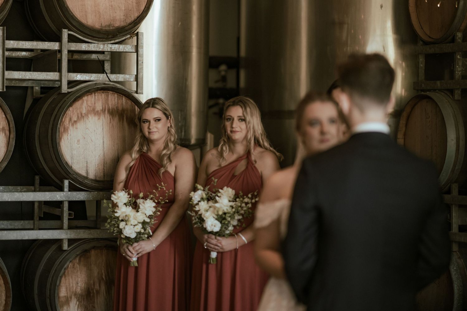 Wedding ceremony in progress at rustic winery with wine barrel backdrop.