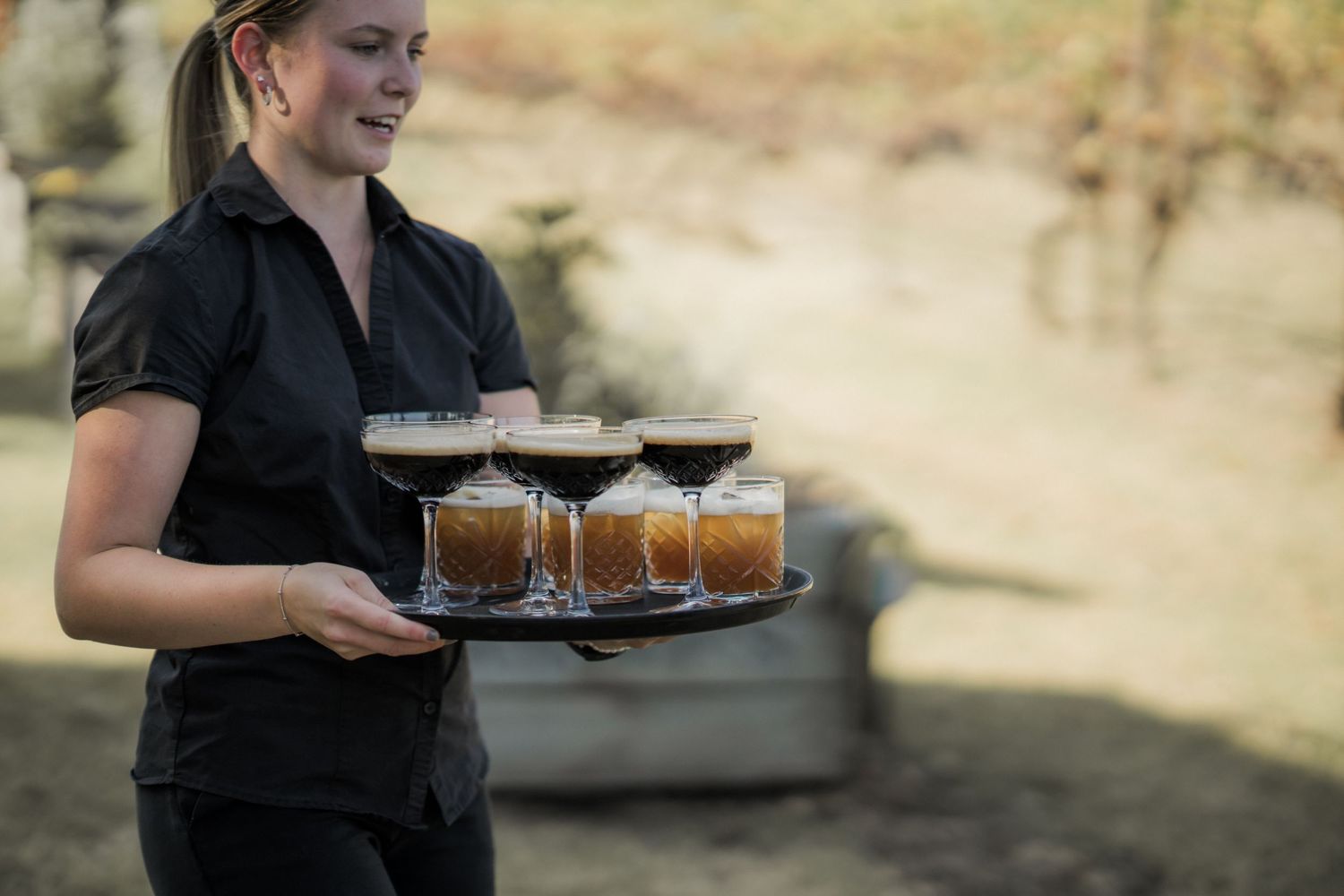 Server carrying a tray of craft beers at an outdoor wedding event.