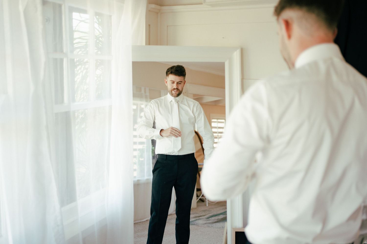 Person adjusting tie while looking in mirror during wedding preparation.