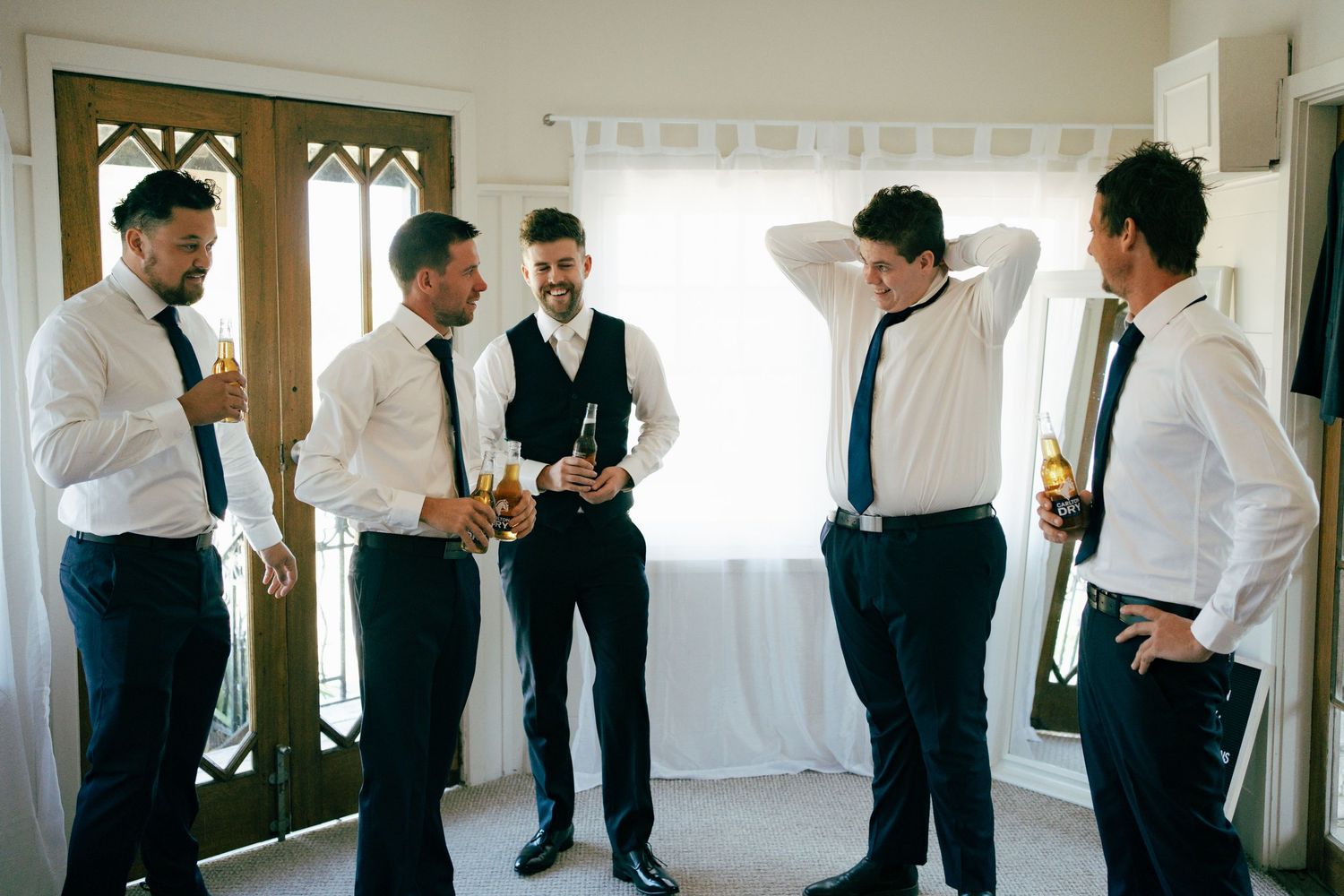 Groomsmen in formal attire sharing a lighthearted moment together before the wedding ceremony.