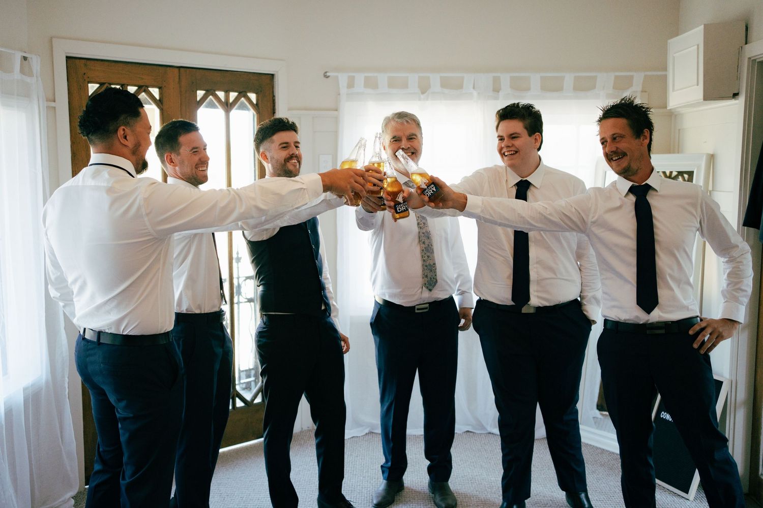 Wedding party members in white shirts and dark pants doing a group fist bump celebration.