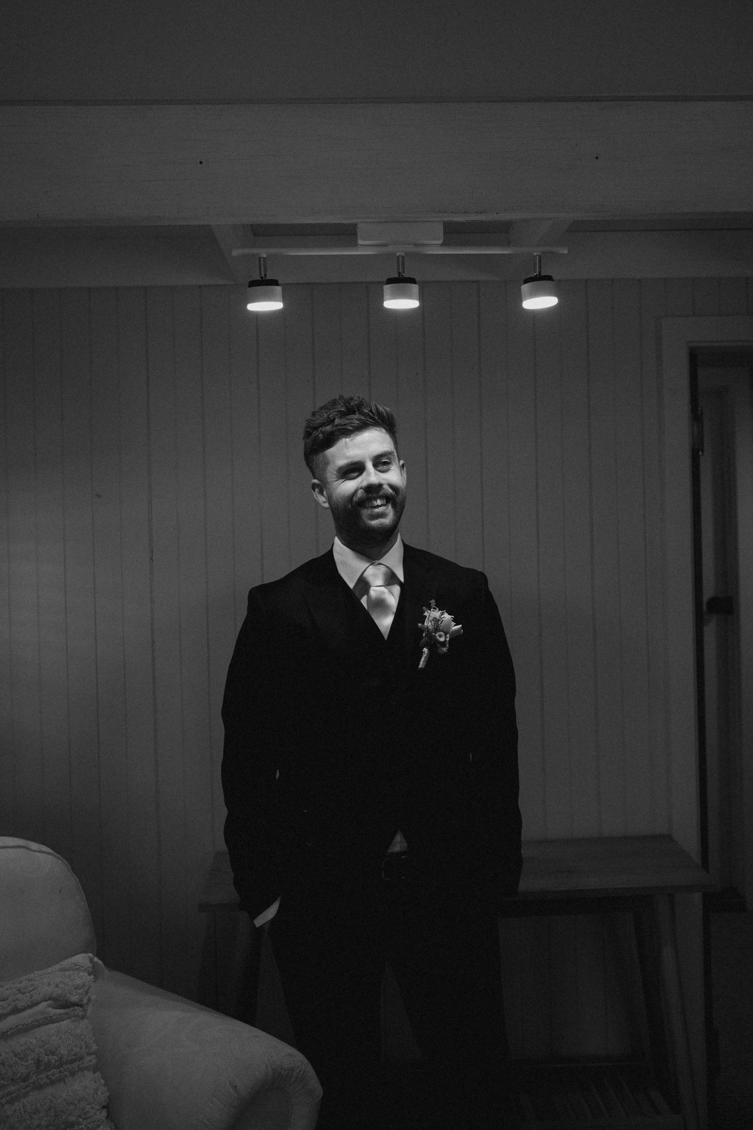 Black and white portrait of groom in formal suit smiling with boutonniere.