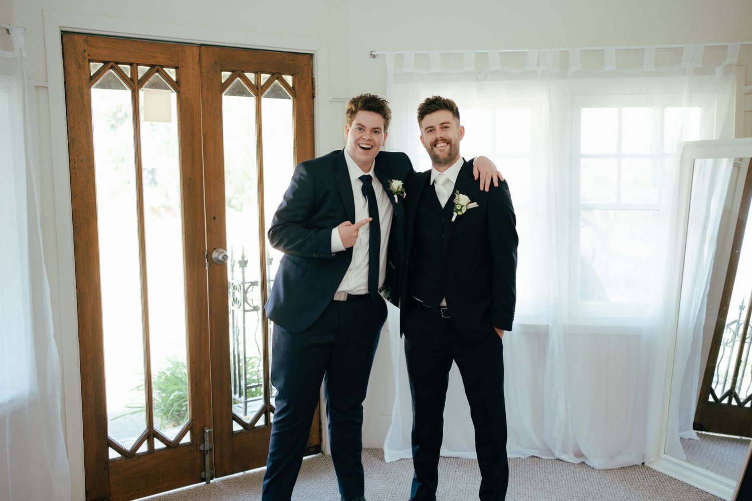 Two people in matching black suits posing together before wedding ceremony.
