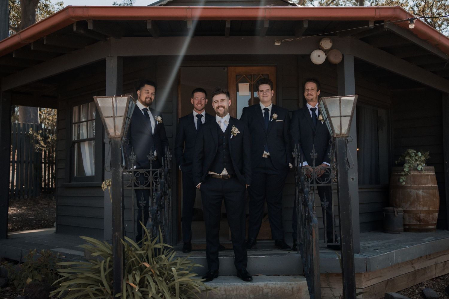 Wedding party in dark suits posing on rustic cabin porch.