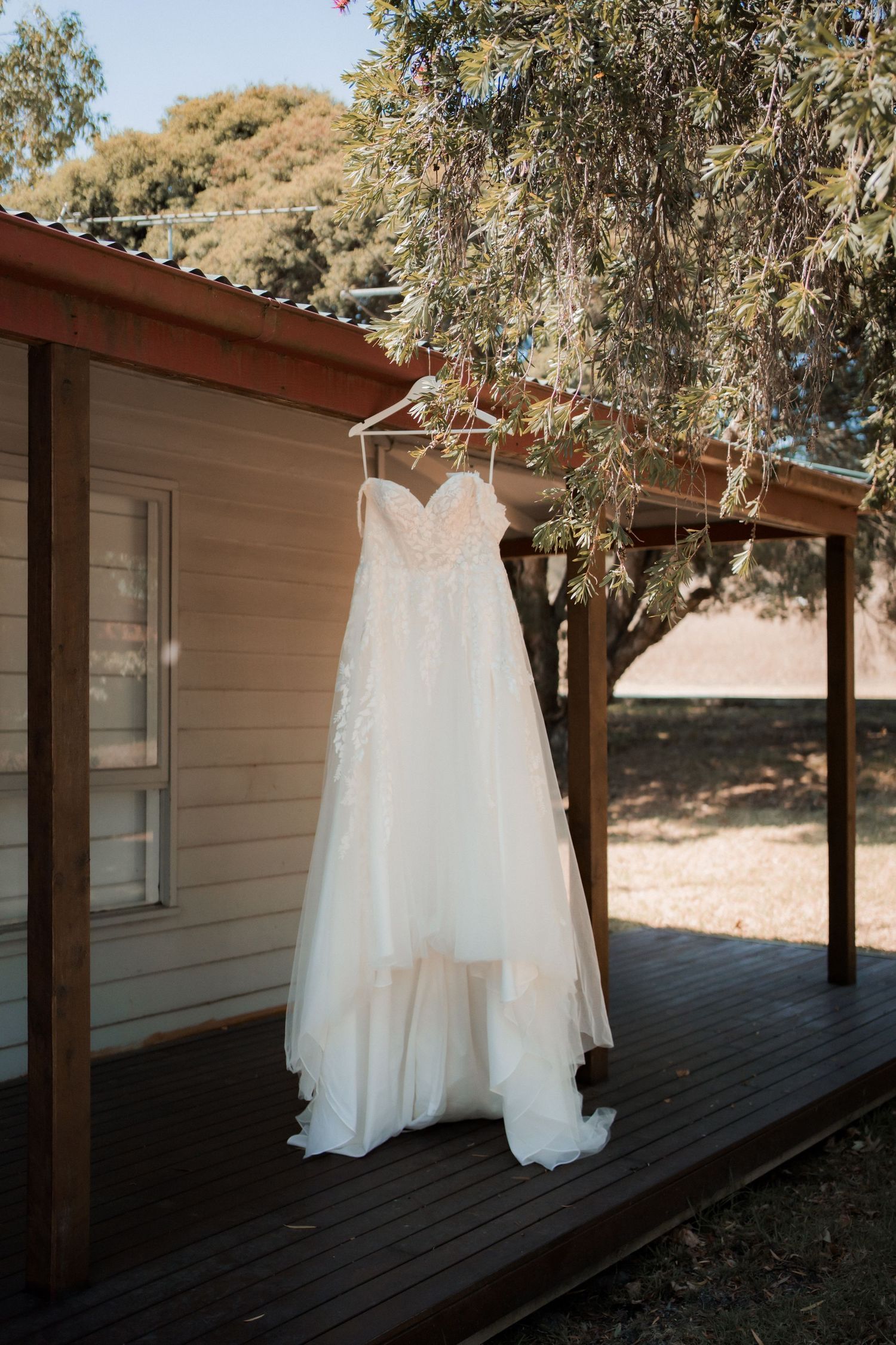 White wedding gown hanging on porch of rustic cabin with trees in background.
