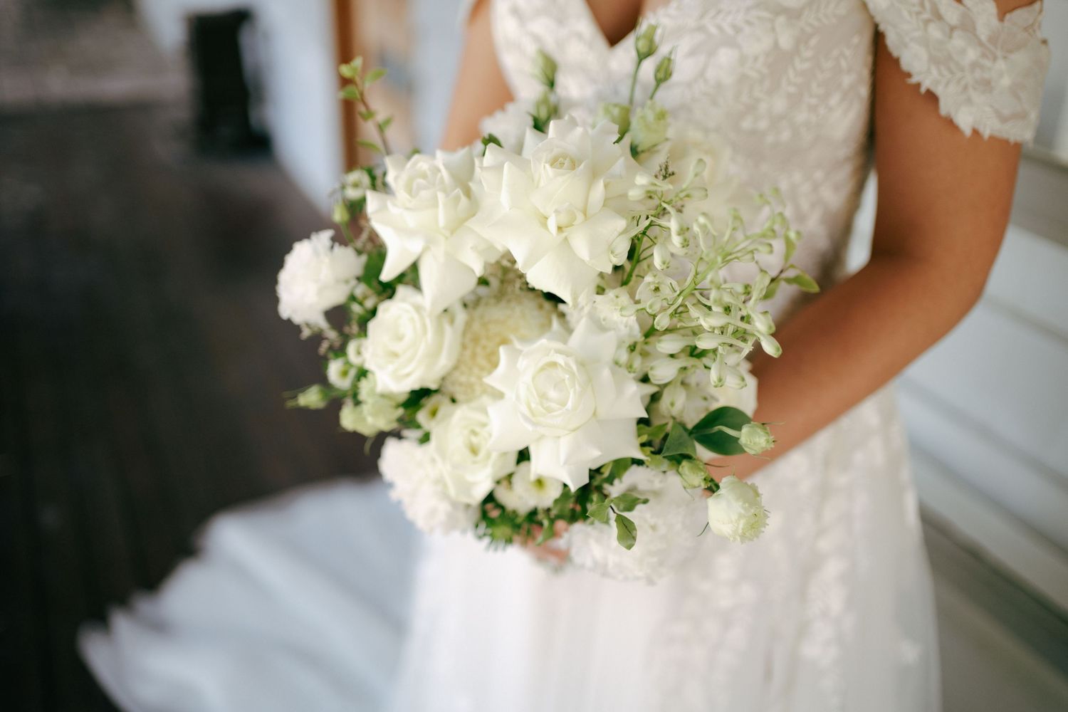 Close up of white and green wedding bouquet with roses against lace wedding dress.