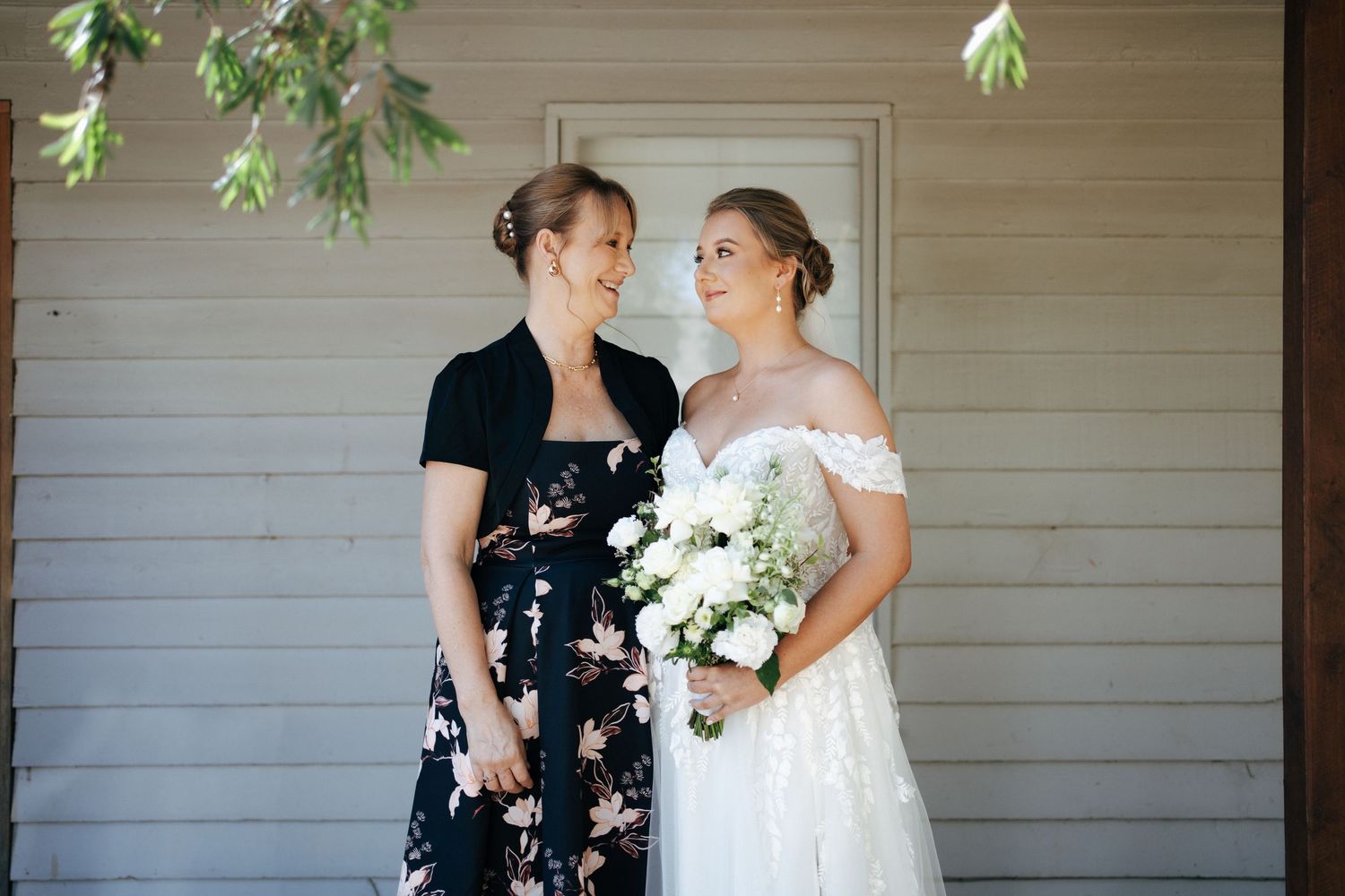 Wedding pair share a moment on rustic porch with white floral bouquet.