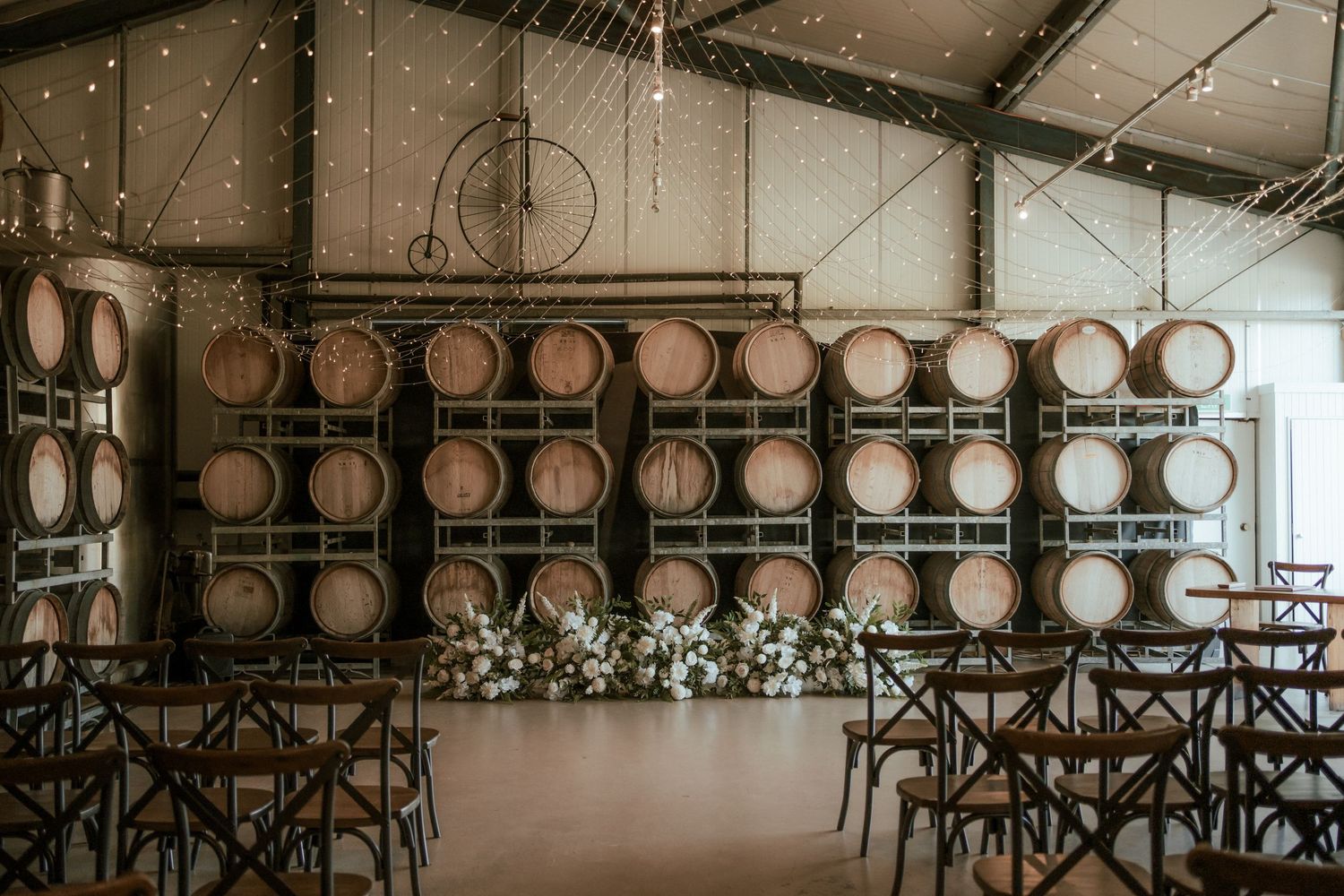 Wedding ceremony setup with wooden barrels and string lights in a rustic winery venue.