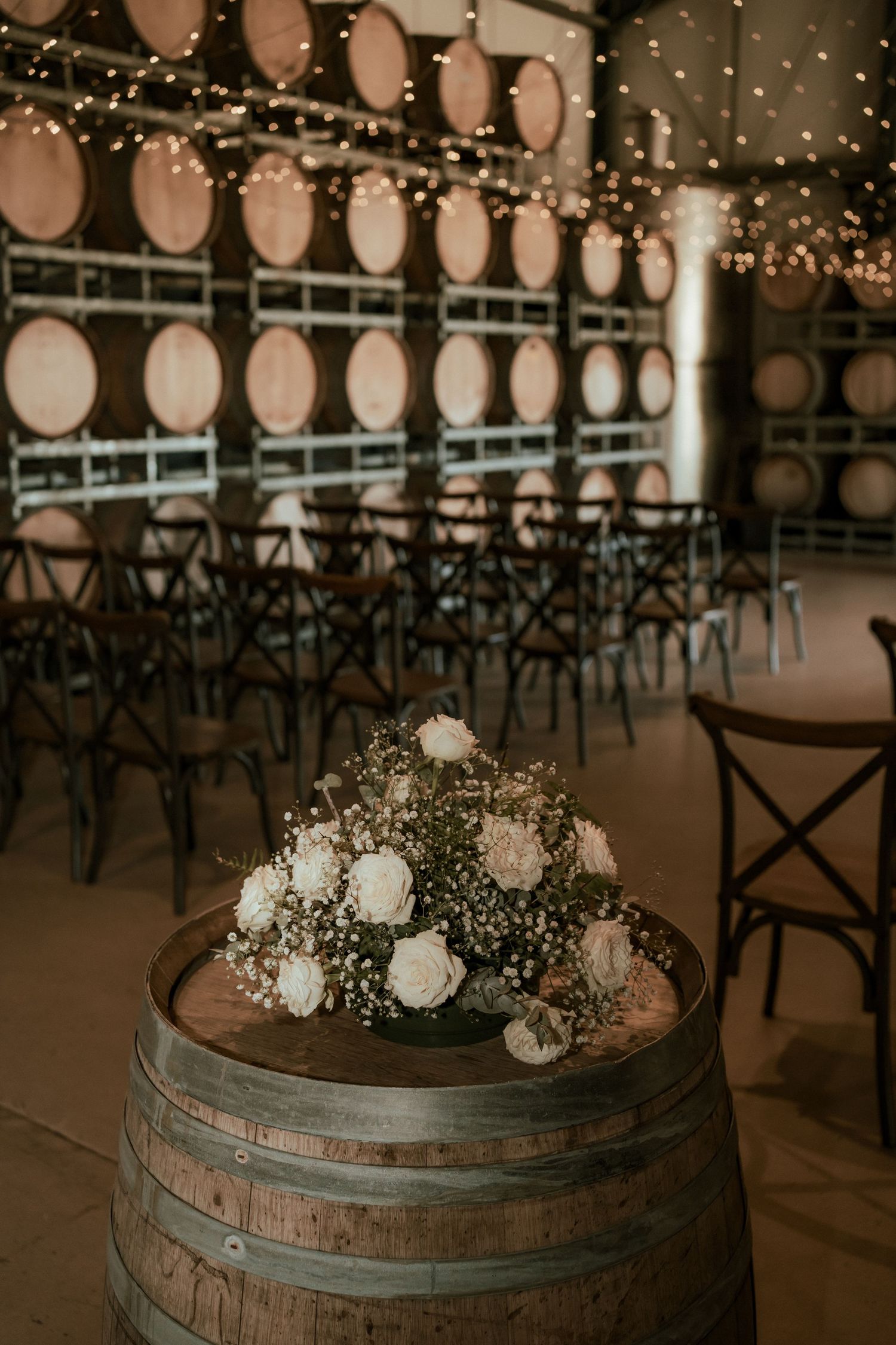 Romantic wedding reception decor with string lights and wine barrels in a rustic venue.