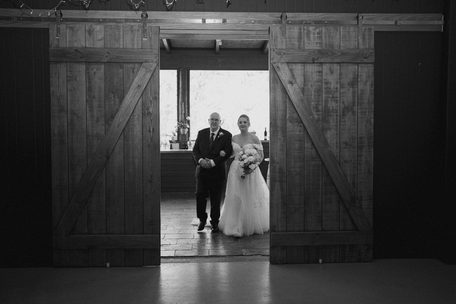 Black and white photo of a wedding entrance through rustic barn doors.