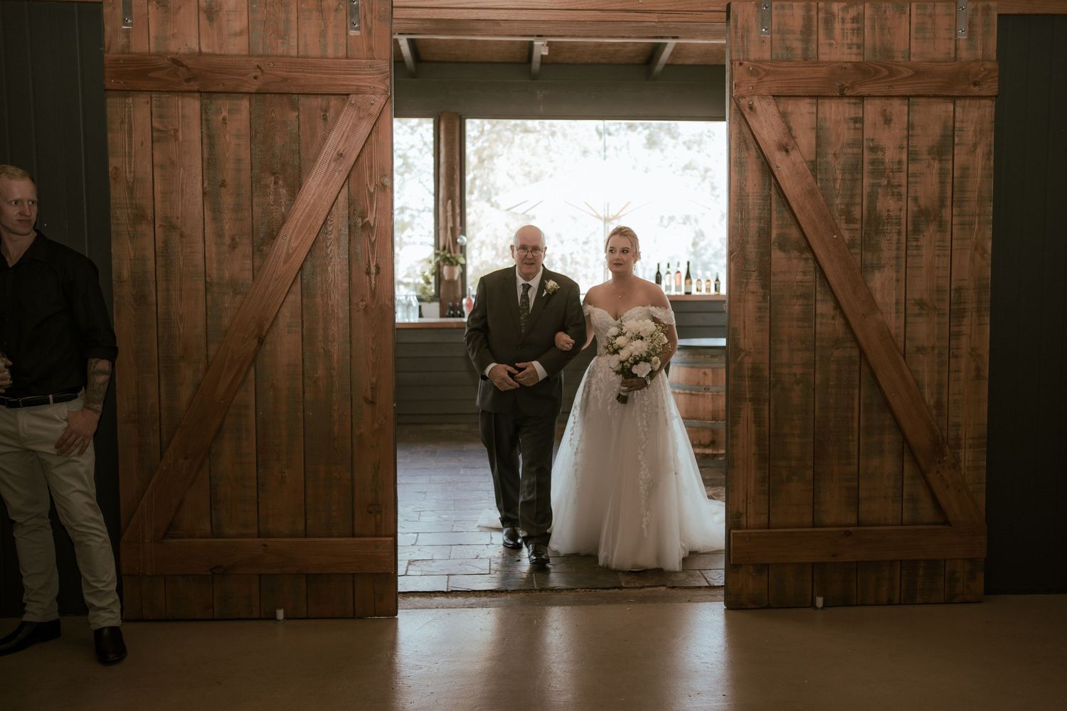 Wedding ceremony entrance through wooden barn doors in a rustic venue.