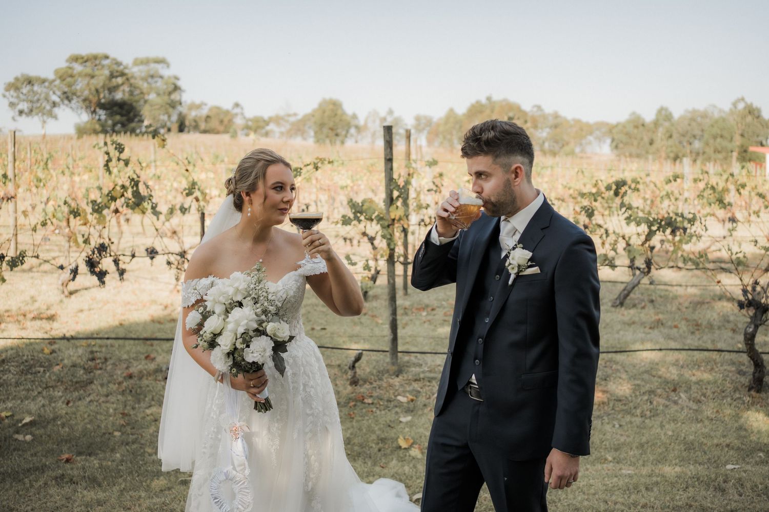 Newlyweds sharing drinks in a vineyard during their wedding celebration.