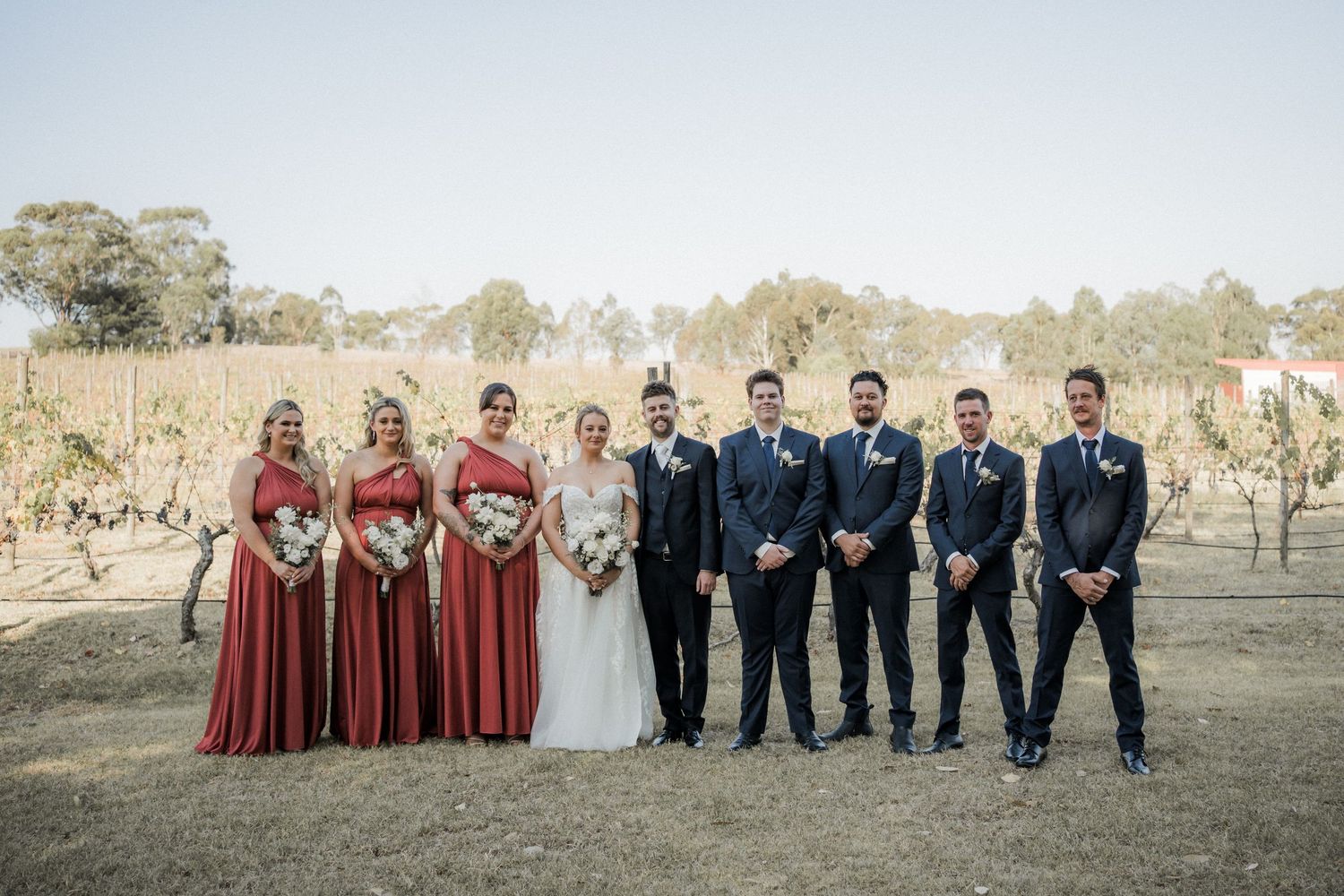 Wedding party portrait in a vineyard with burgundy bridesmaids dresses and navy suits.