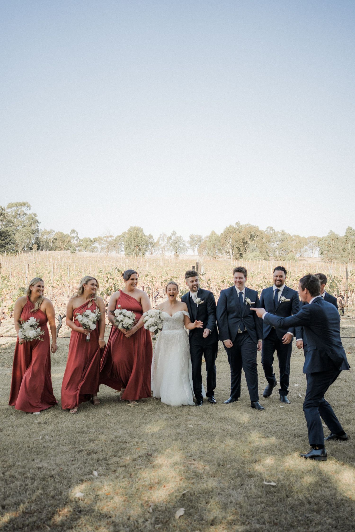 Candid moment of wedding party laughing together in a vineyard setting.