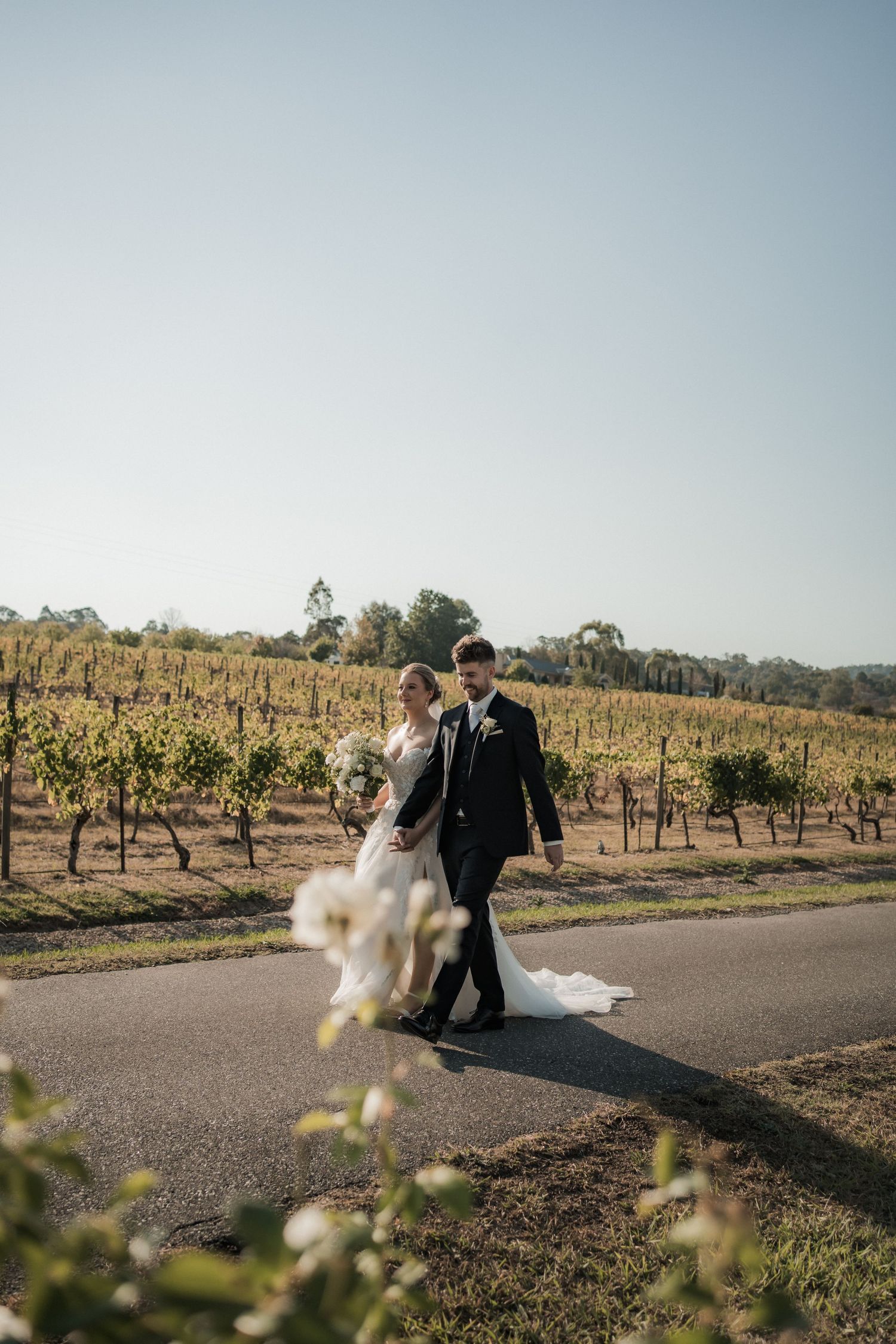 Couple walking through vineyard with dress flowing in breeze during sunset.