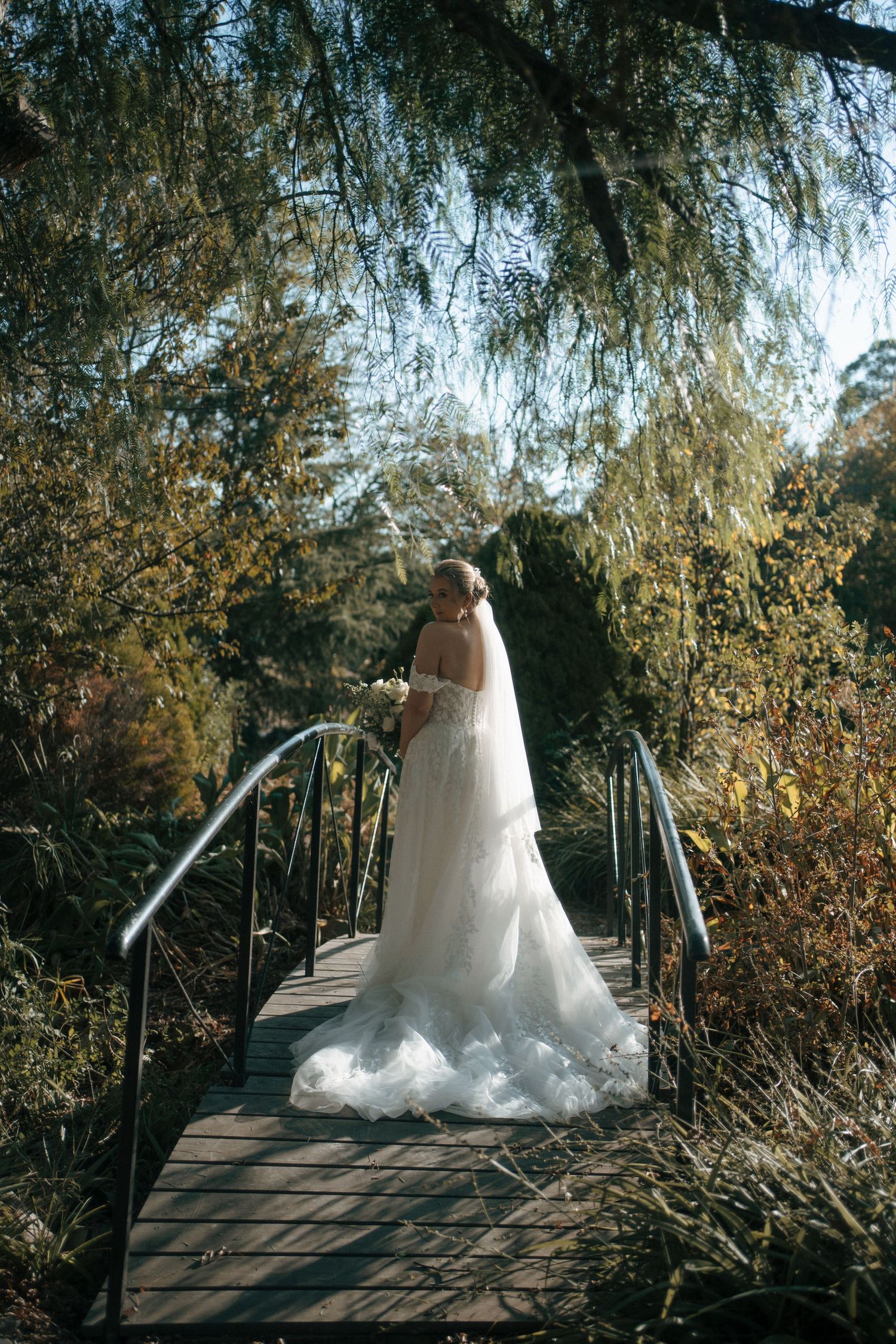 Stunning bridal portrait on a wooden bridge surrounded by willow trees.