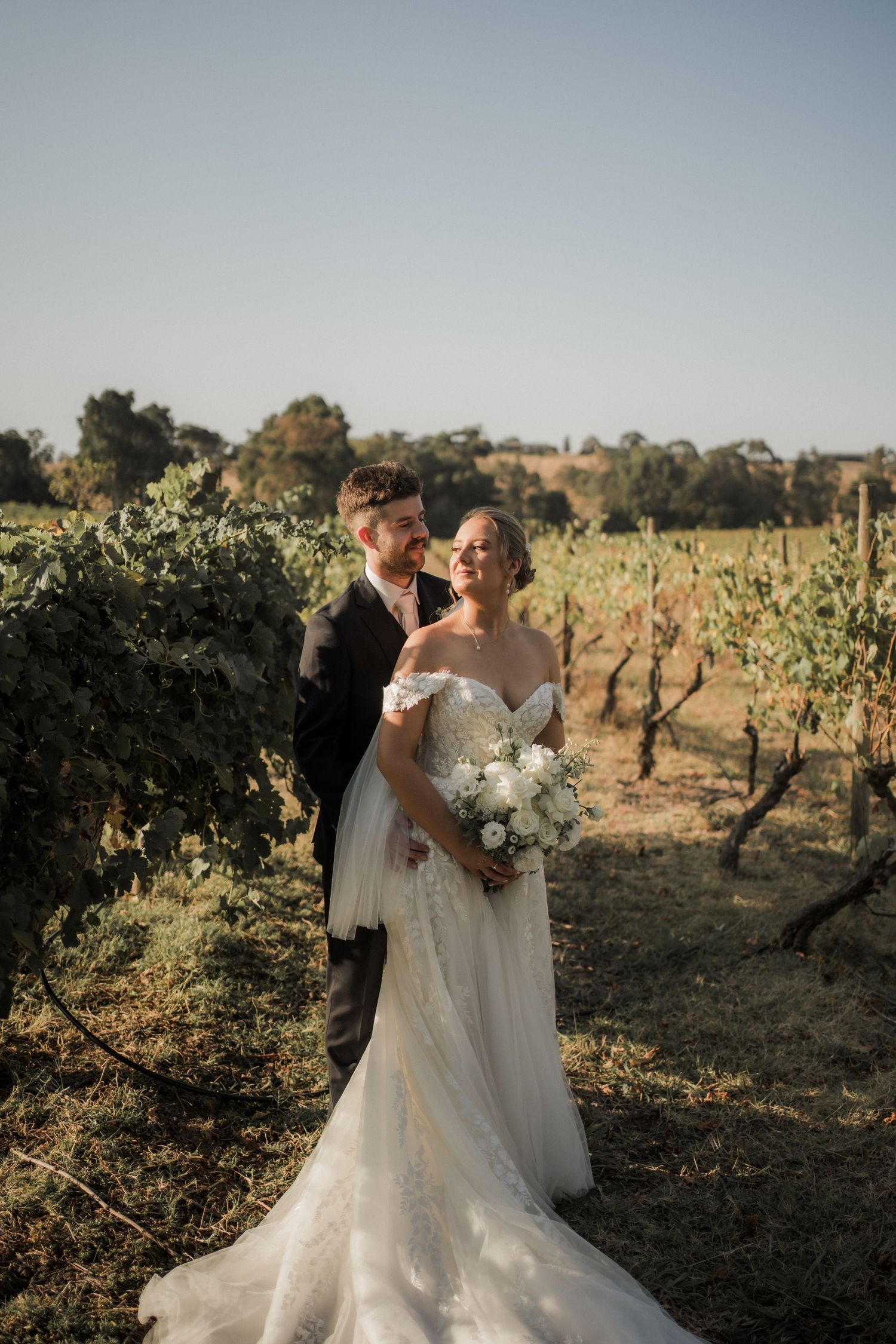 Romantic wedding portrait among vineyard rows during golden hour.