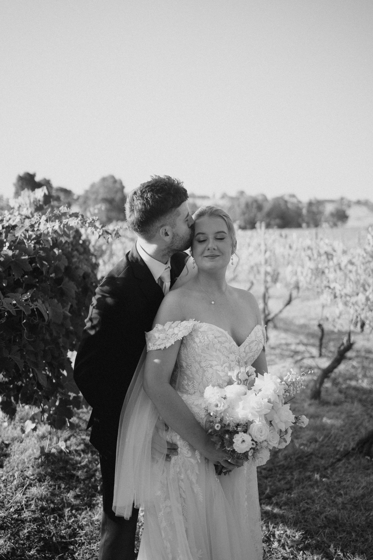 Intimate black and white portrait in a vineyard with delicate white bouquet.