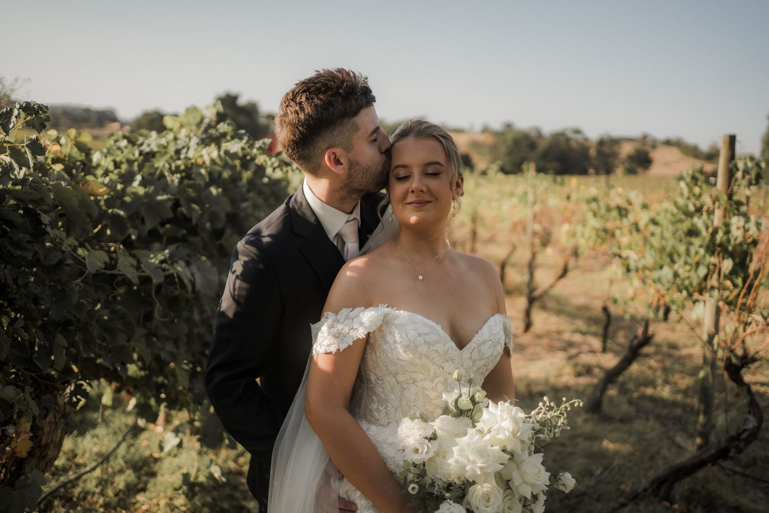 Intimate moment captured between newlyweds in a sun-drenched vineyard setting.