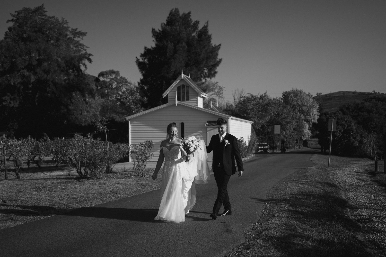Wedding couple walking away from a white chapel building in black and white photography.