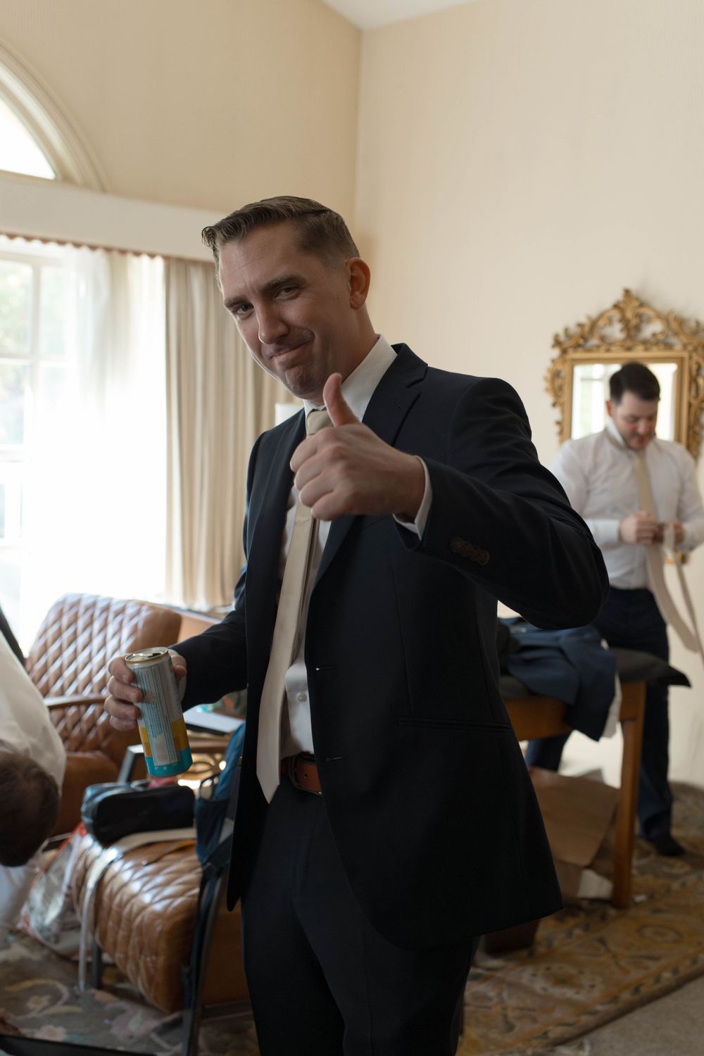 A well-dressed person gives a thumbs up gesture while getting ready in a furnished room.
