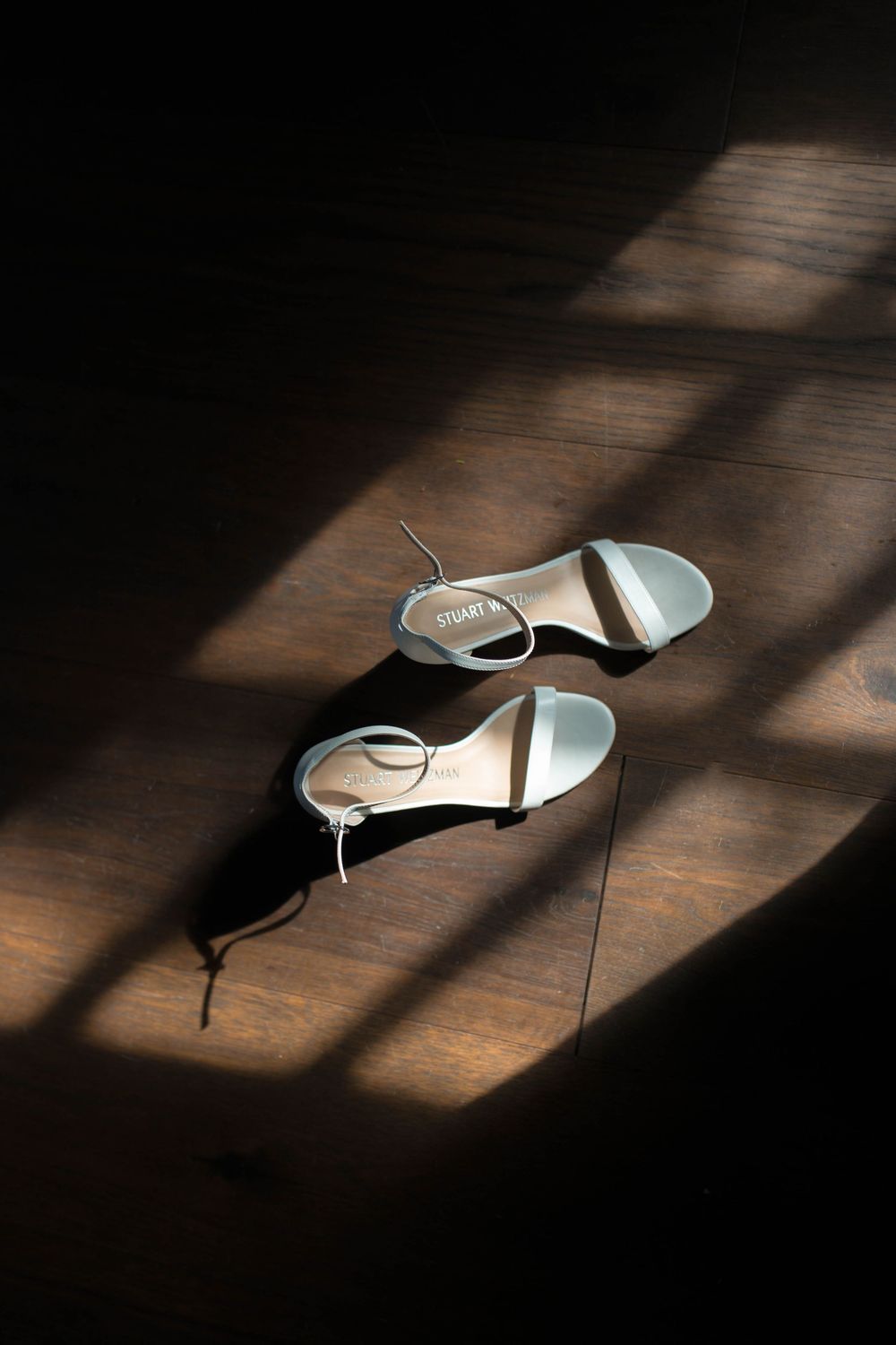 White bridal shoes cast dramatic shadows on a wooden floor in natural window light.