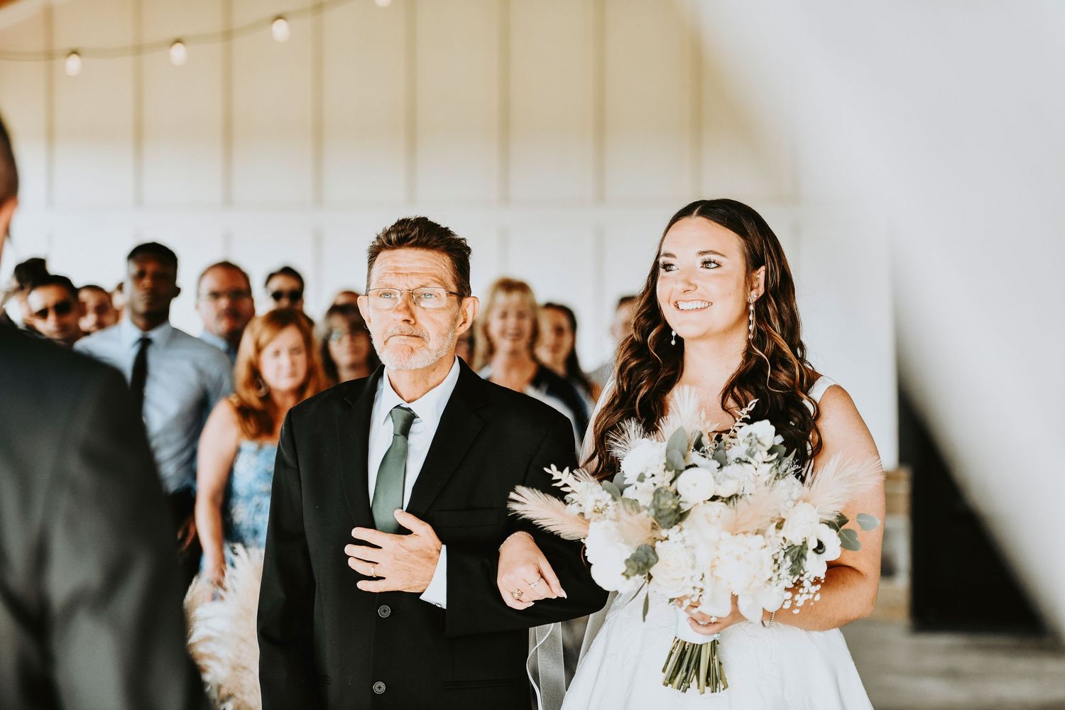 Bride holding bouquet at altar under barn pavilion as she walks down the aisle with her father