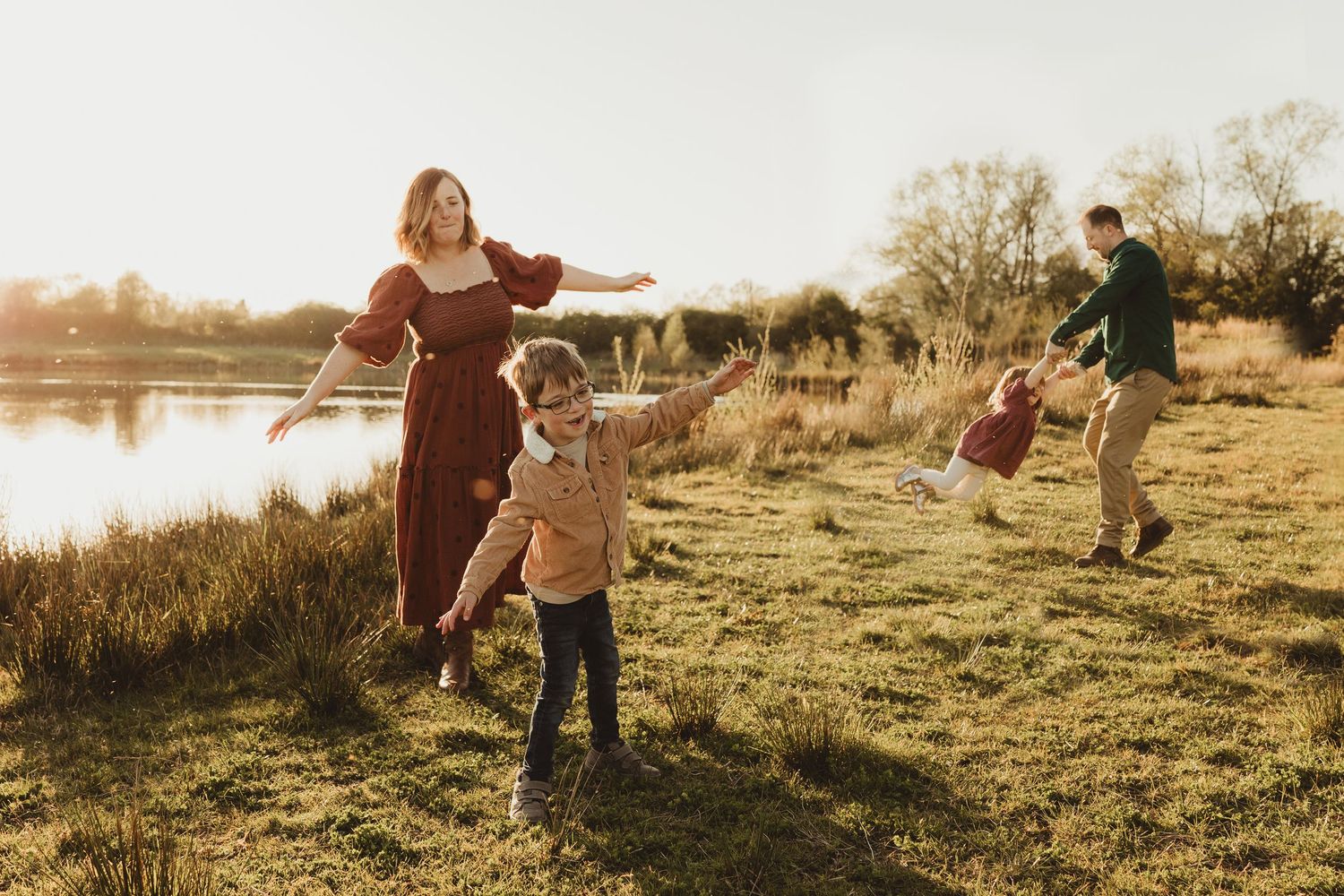 Two young children laugh and play together in a grassy field at golden hour near a pond.