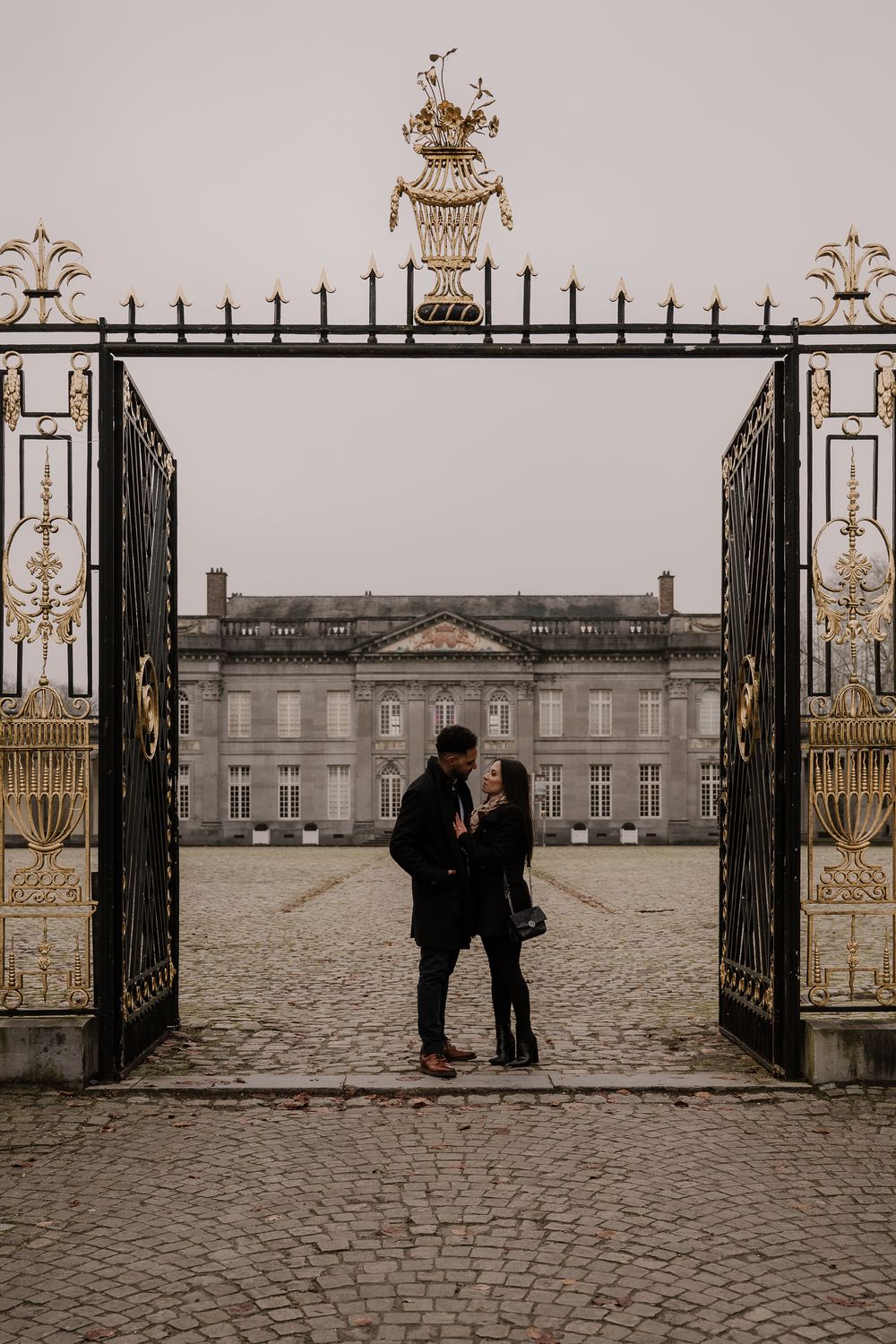Romantic silhouette of two people framed by ornate golden gates at an elegant European palace entrance.