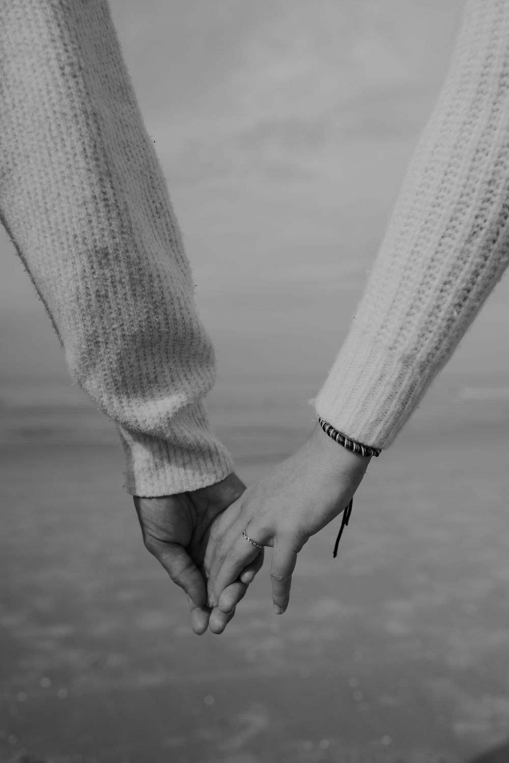 A black and white close-up of two people holding hands while wearing cozy knit sweaters.