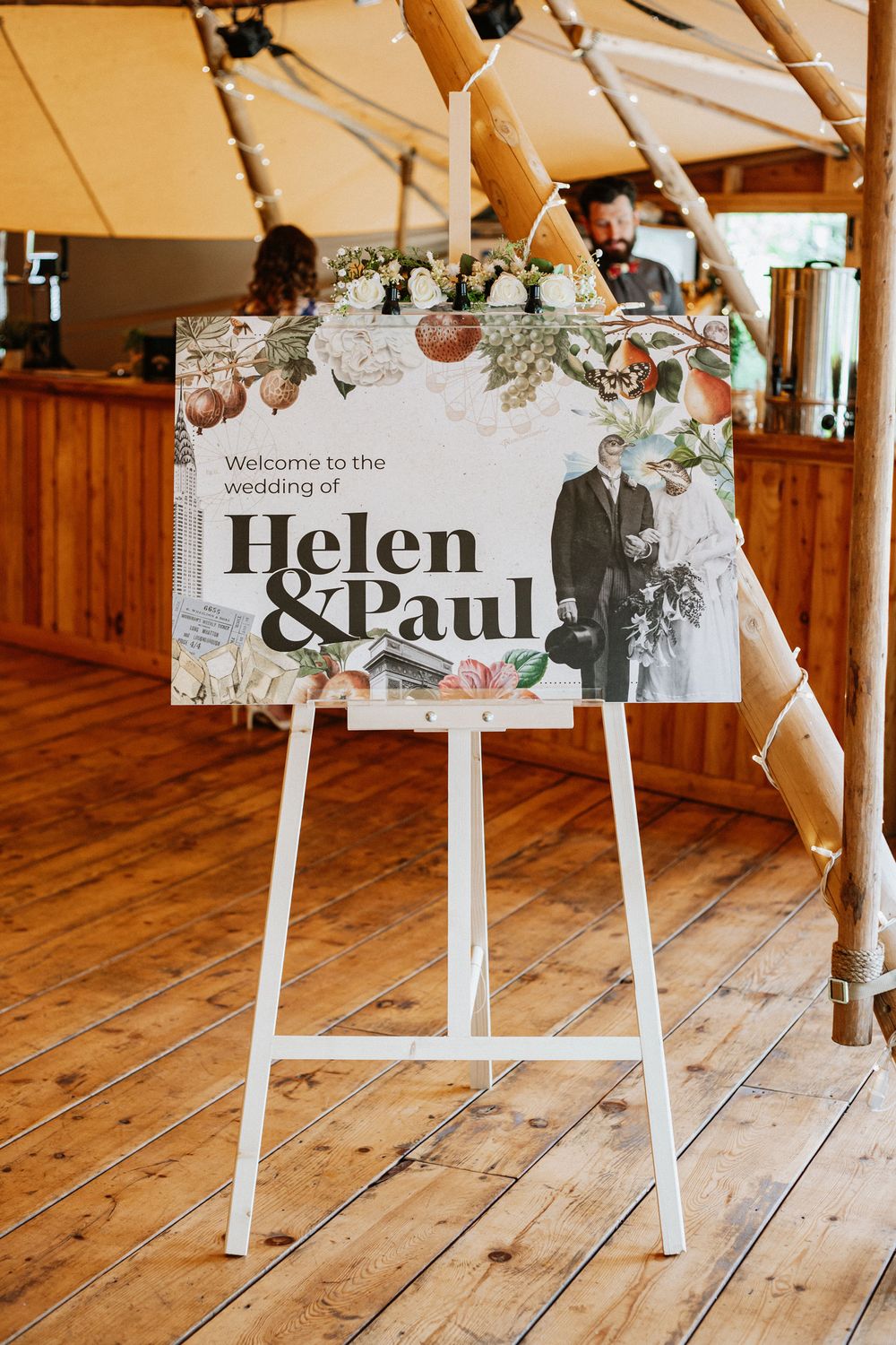 An elegant wedding welcome sign on a white easel features floral decorations and text in a rustic wooden venue.