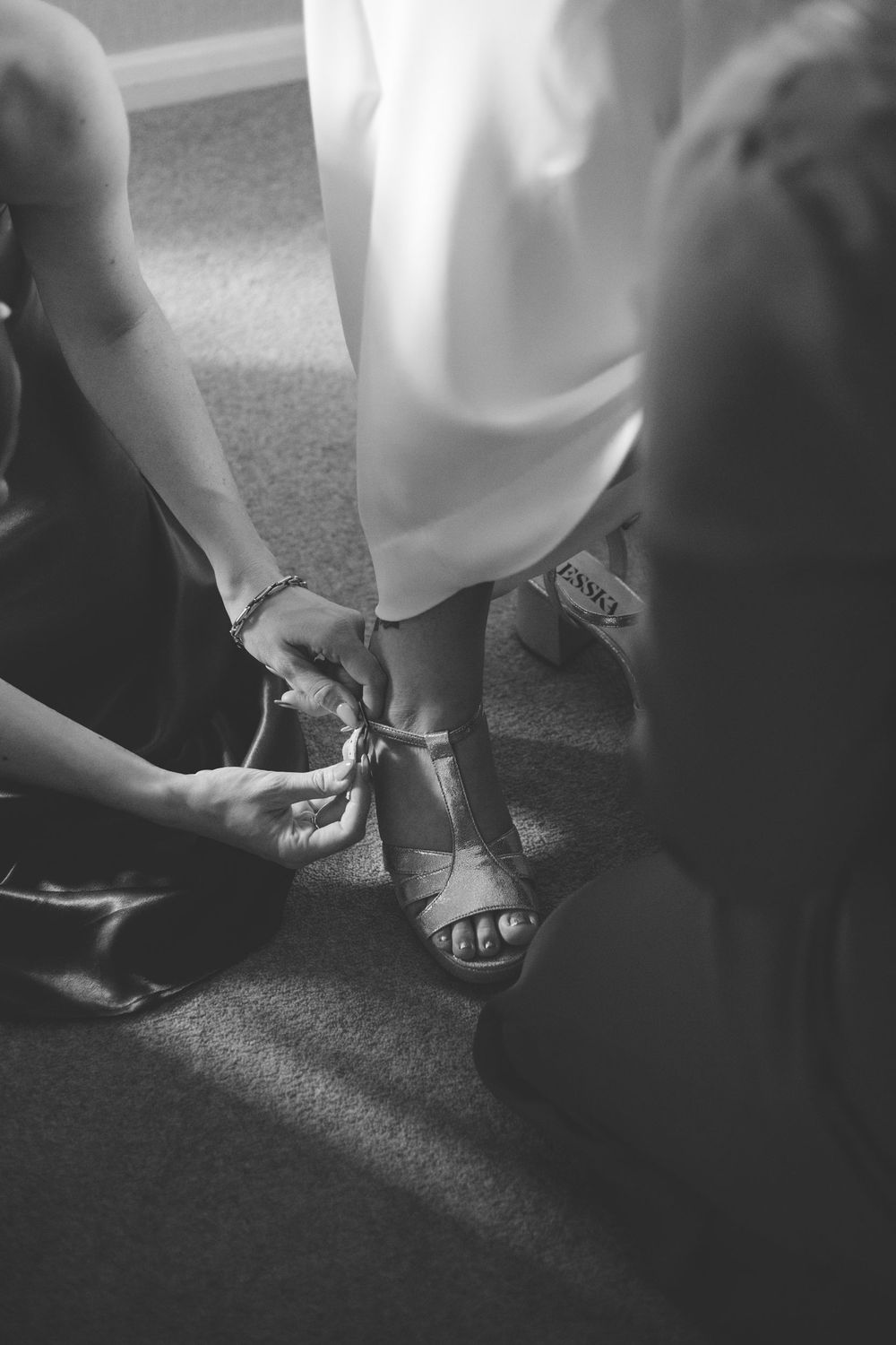 Black and white photograph of hands adjusting the strap of a sandal during a formal occasion.