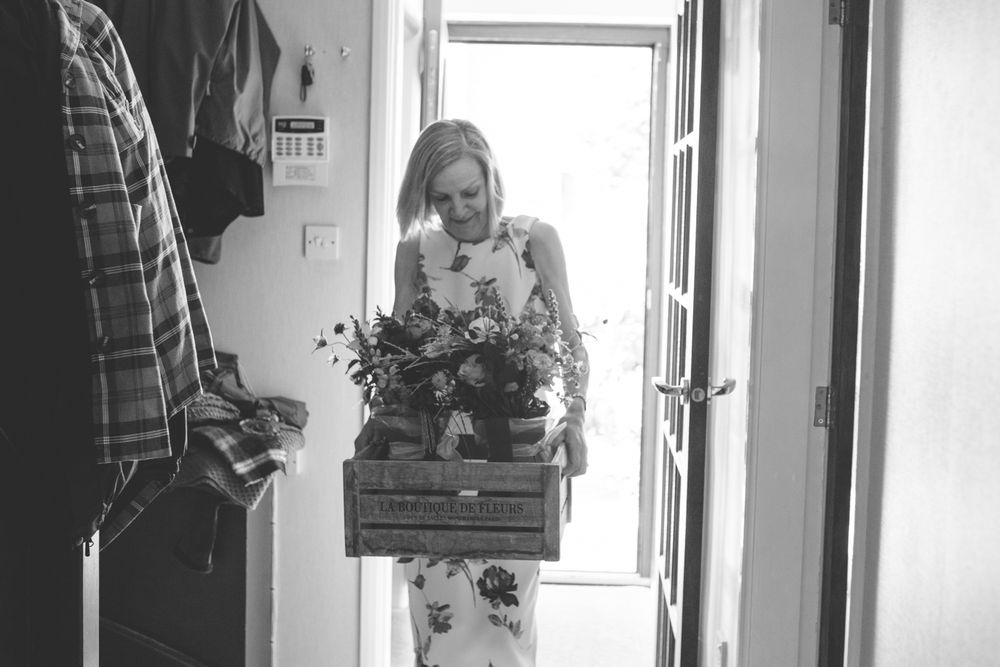 Black and white photo of someone carrying a wooden crate filled with flowers through a doorway.