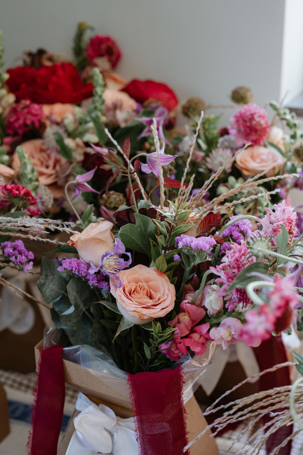 Beautiful floral centerpieces with burgundy vases showcase pink roses, pastel blooms and greenery on an elegant tablescape.