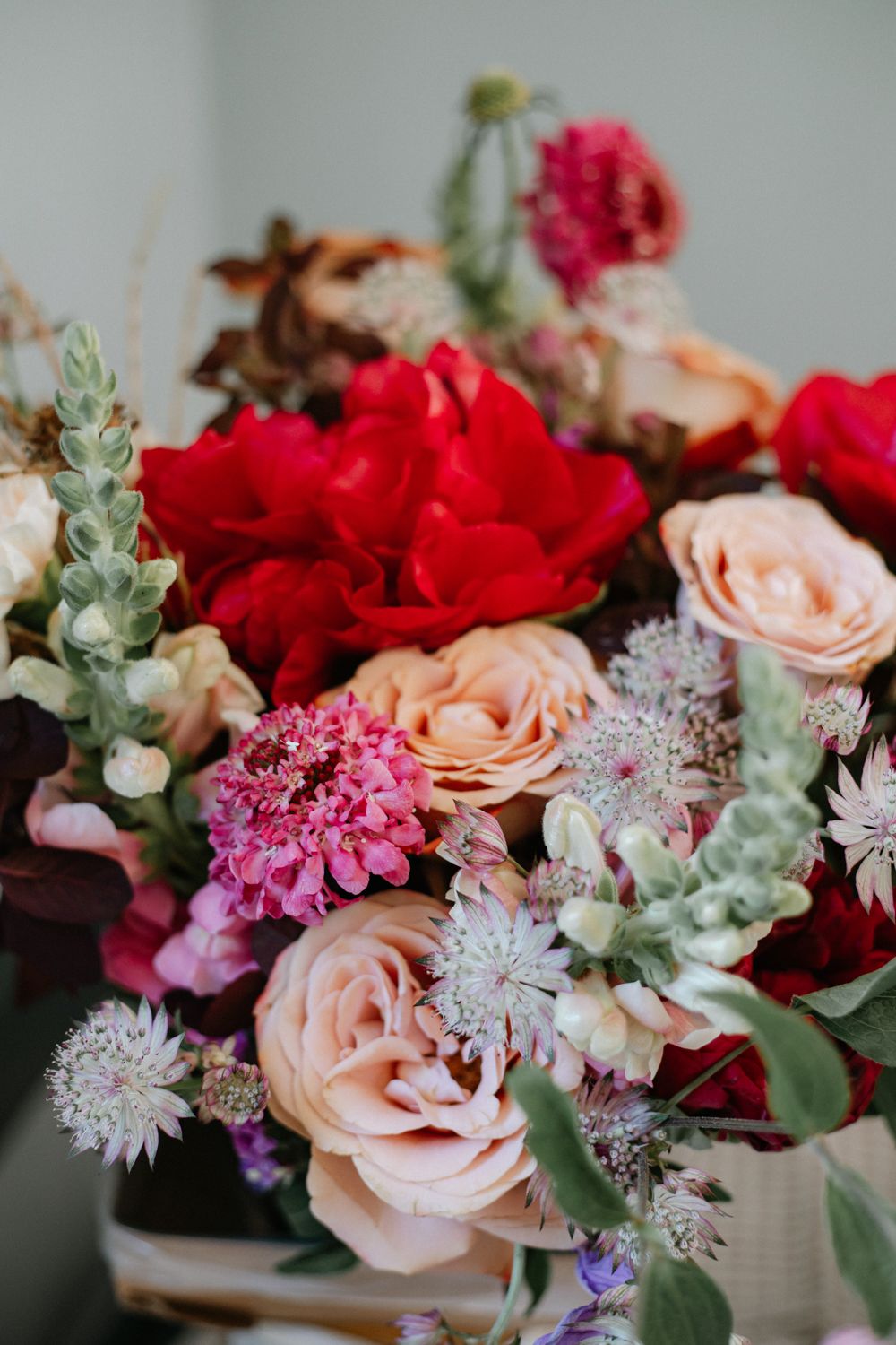 Elegant floral arrangement featuring red and pink roses, pale astilbe, and eucalyptus in a romantic wedding bouquet style.