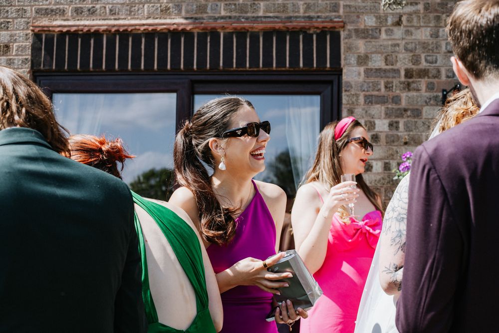 People in colorful summer outfits gathered outside a brick building with sunglasses on a bright sunny day.