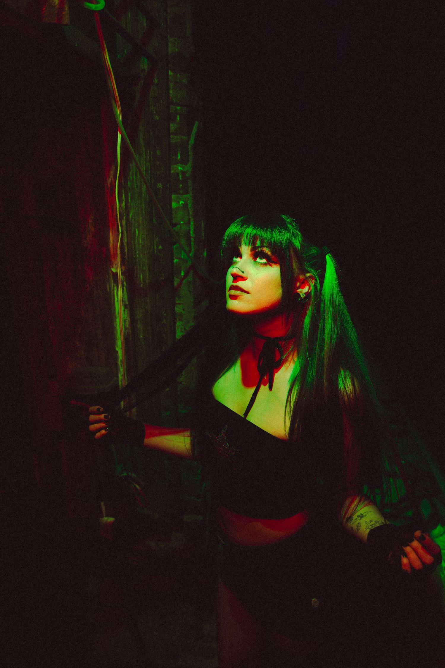 Artistic dark portrait with dramatic green lighting creating a moody gothic atmosphere against black background.