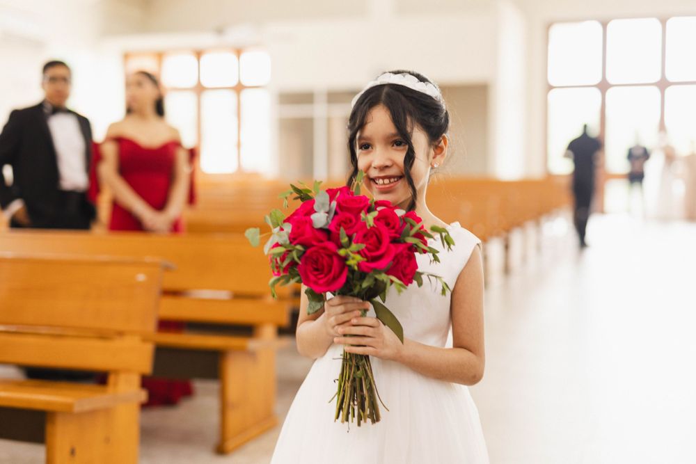 A bride in white holds a striking red bouquet while standing in a sunlit church.