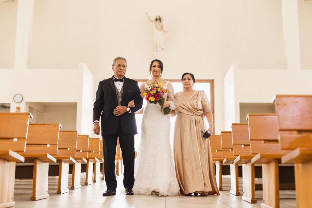 A wedding party walks down the aisle of a bright church with wooden pews.