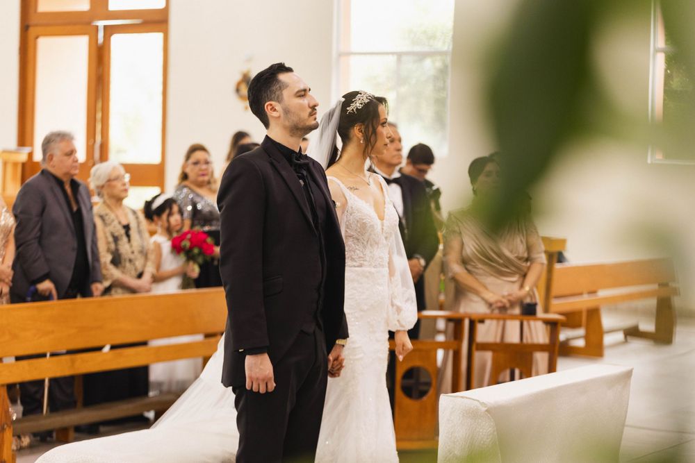A couple stands together during their wedding ceremony in a sunlit church sanctuary.