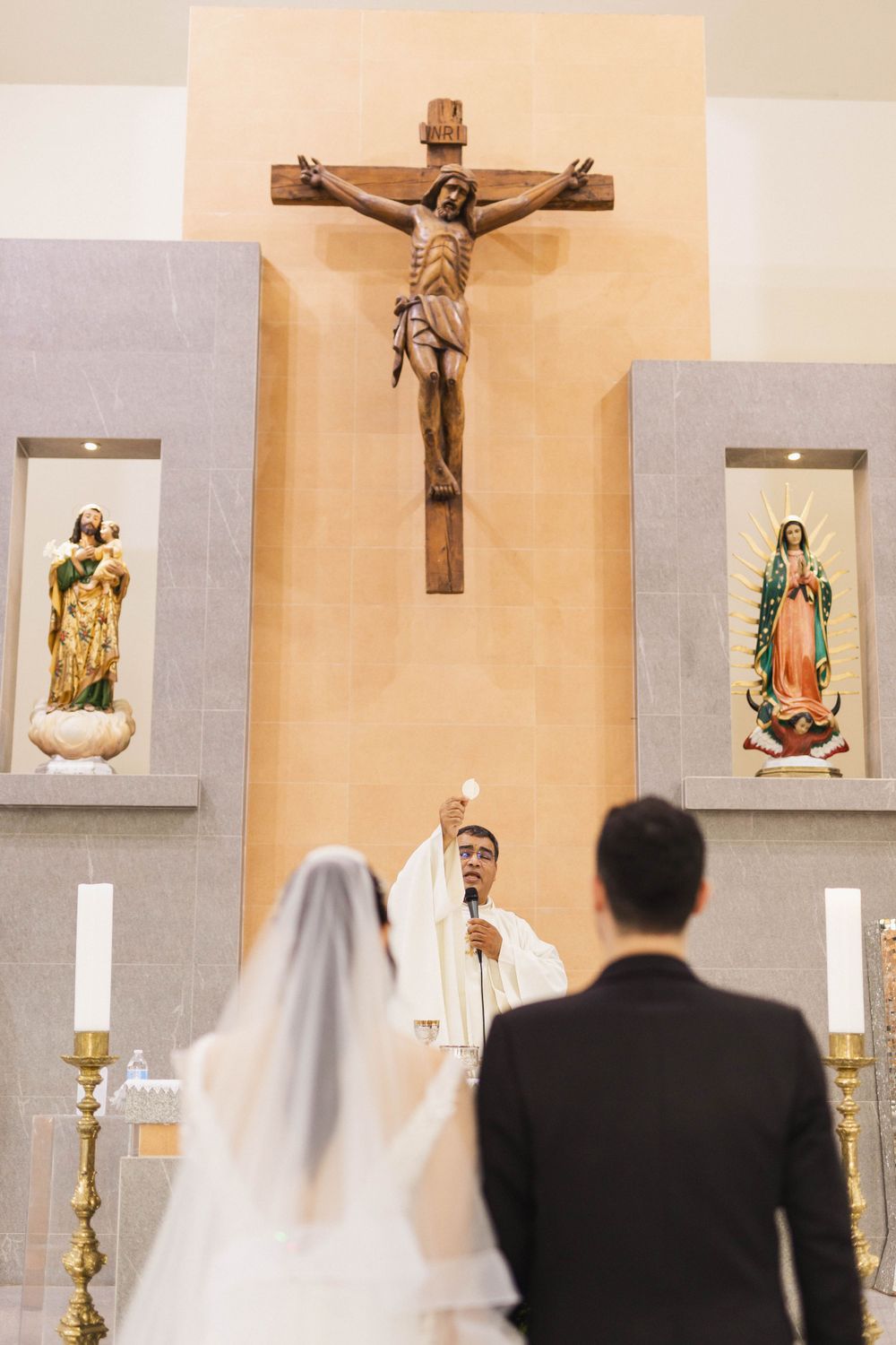 A Catholic wedding ceremony before a large crucifix with religious icons on either side.