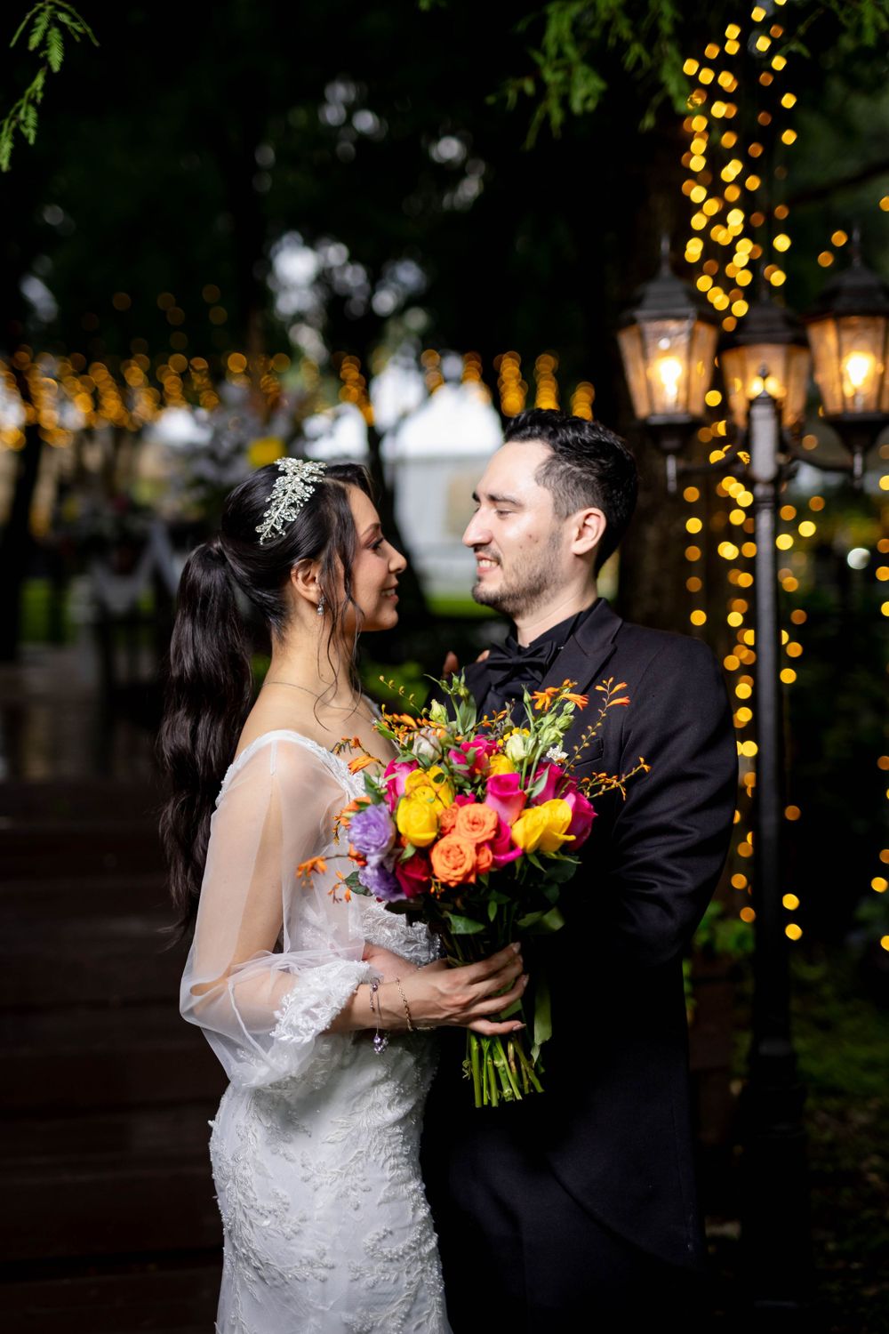 Evening wedding portrait with vibrant bouquet and string lights creating warm ambiance.