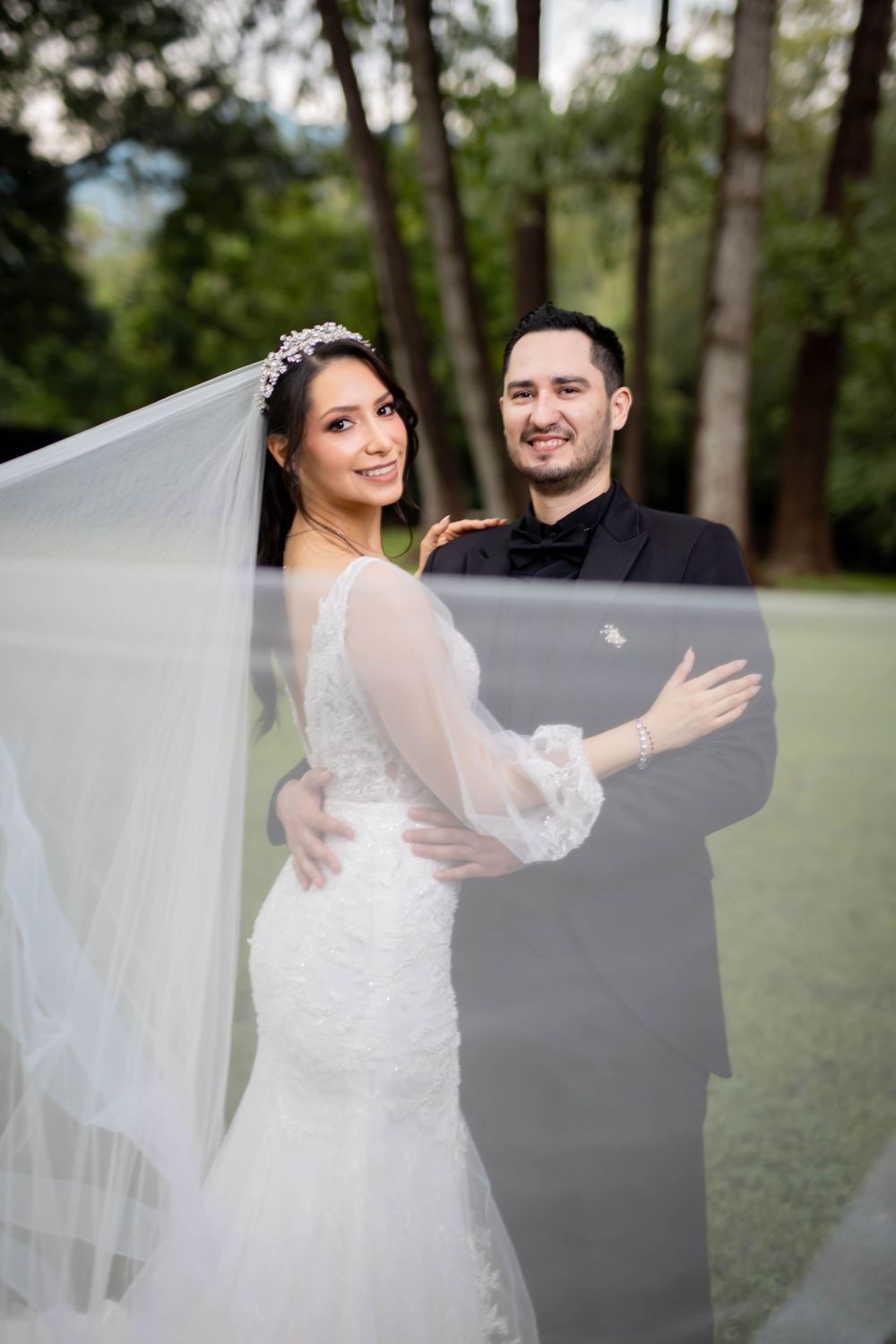 A romantic wedding portrait of a couple in a wooded setting with the bride wearing a flowing veil.