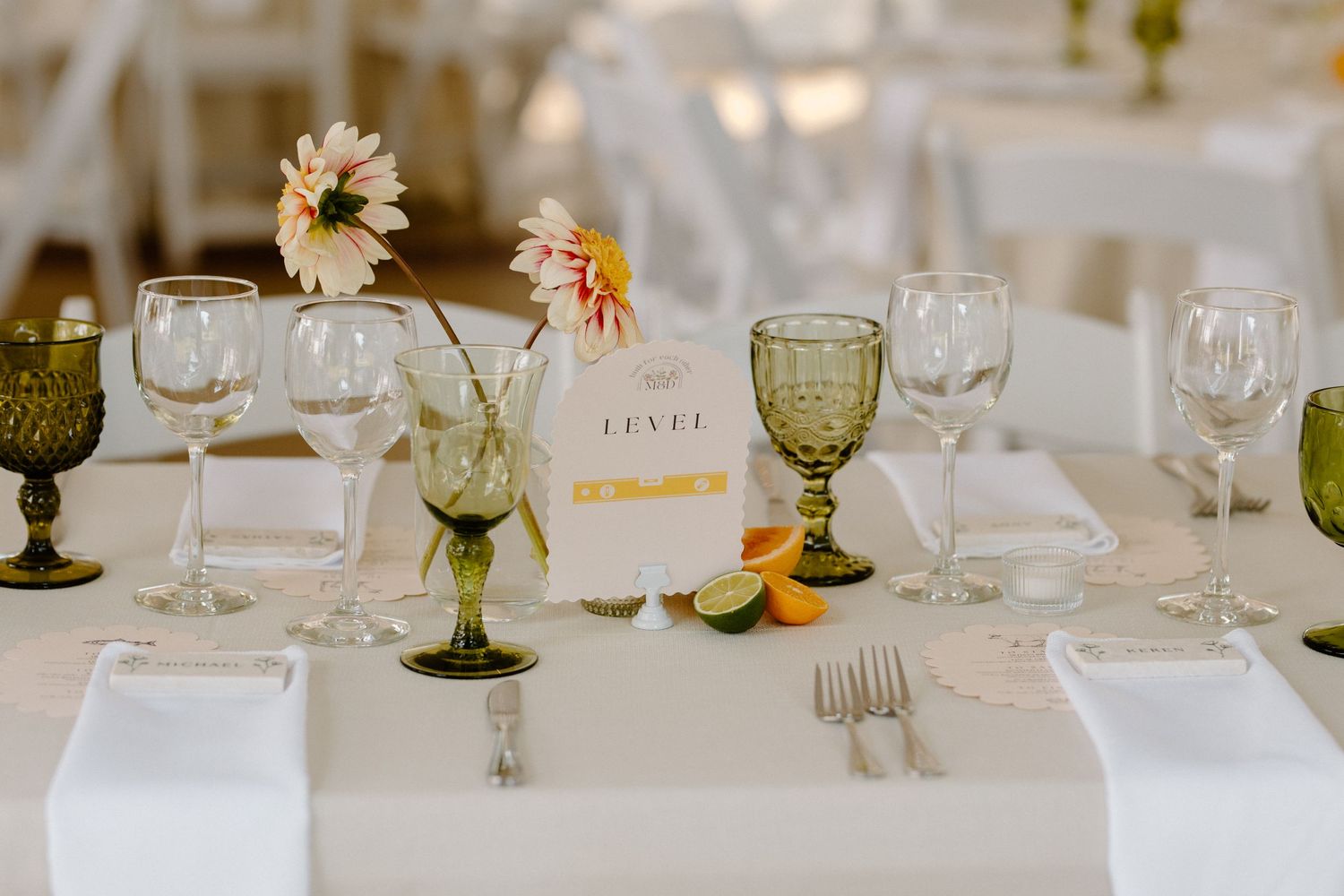 Elegant wedding table setting with green goblets, white linens, and delicate daisies in small vase centerpieces.