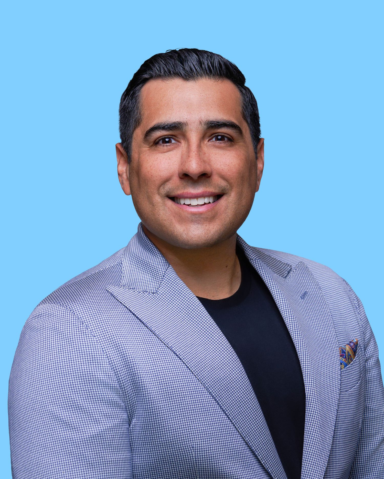 Professional headshot in gray blazer against blue background.