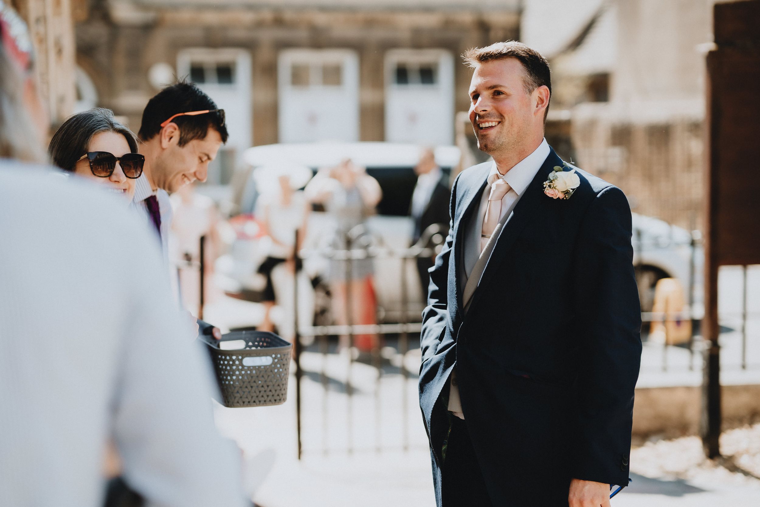 Groom in a black suit and tie smiles at ceremony location during outdoor winter wedding.