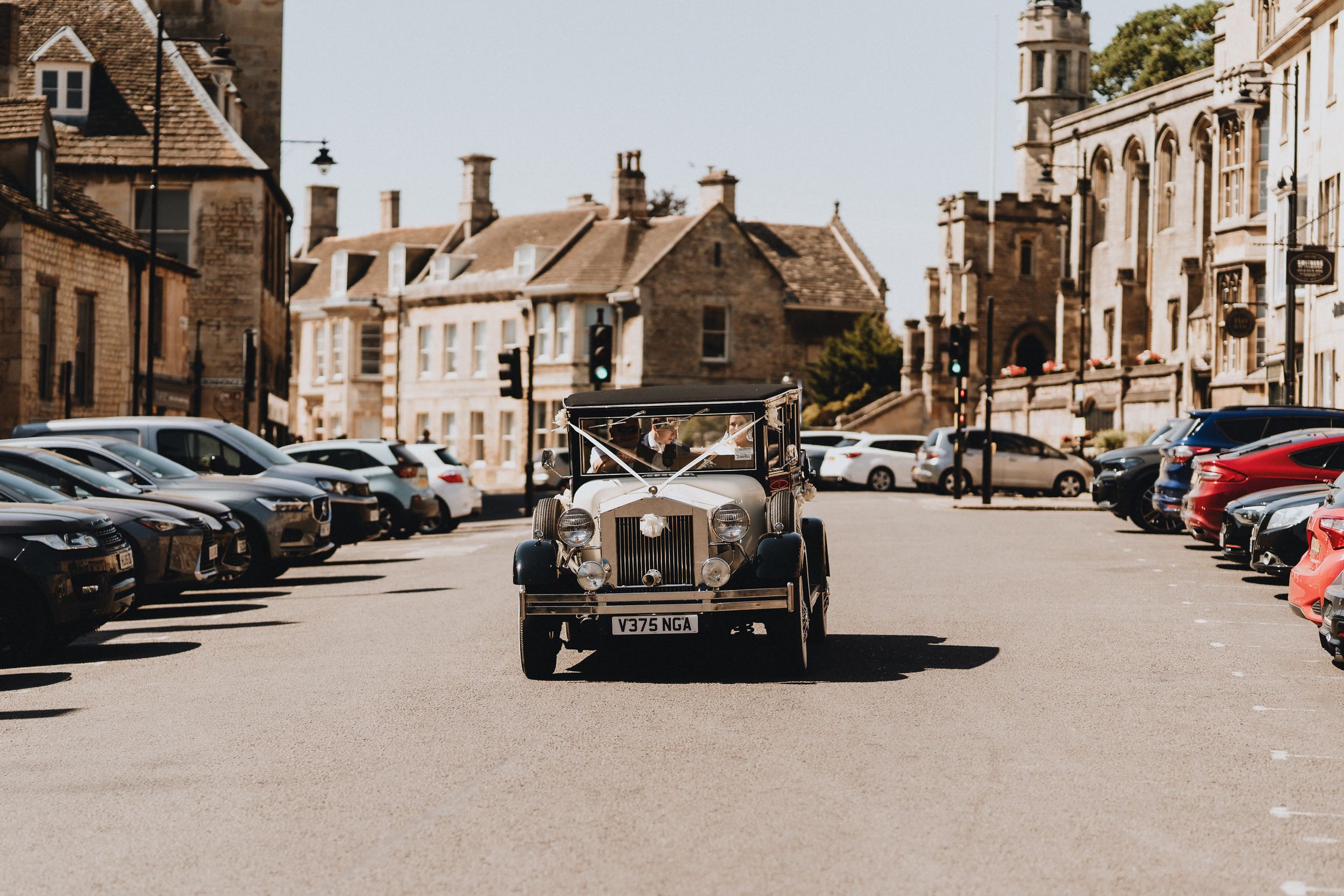 Vintage MG classic car driving down charming stone street in Stamford with parked cars and historic buildings in English town.
