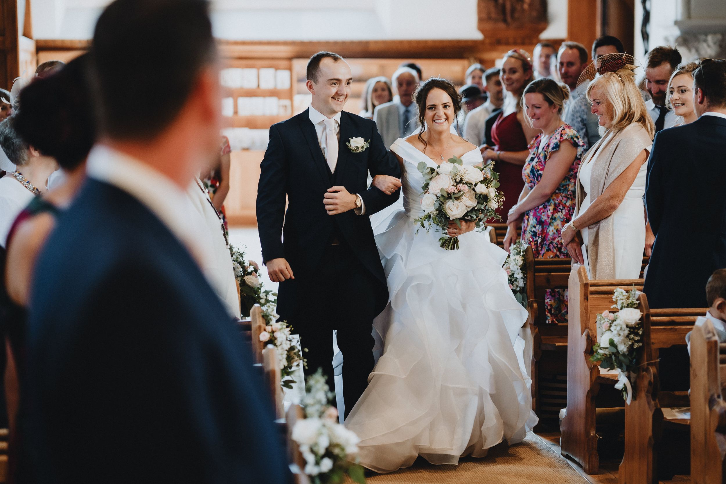 A beautiful church wedding ceremony with white floral decorations along the aisle as couple walks down during processional.