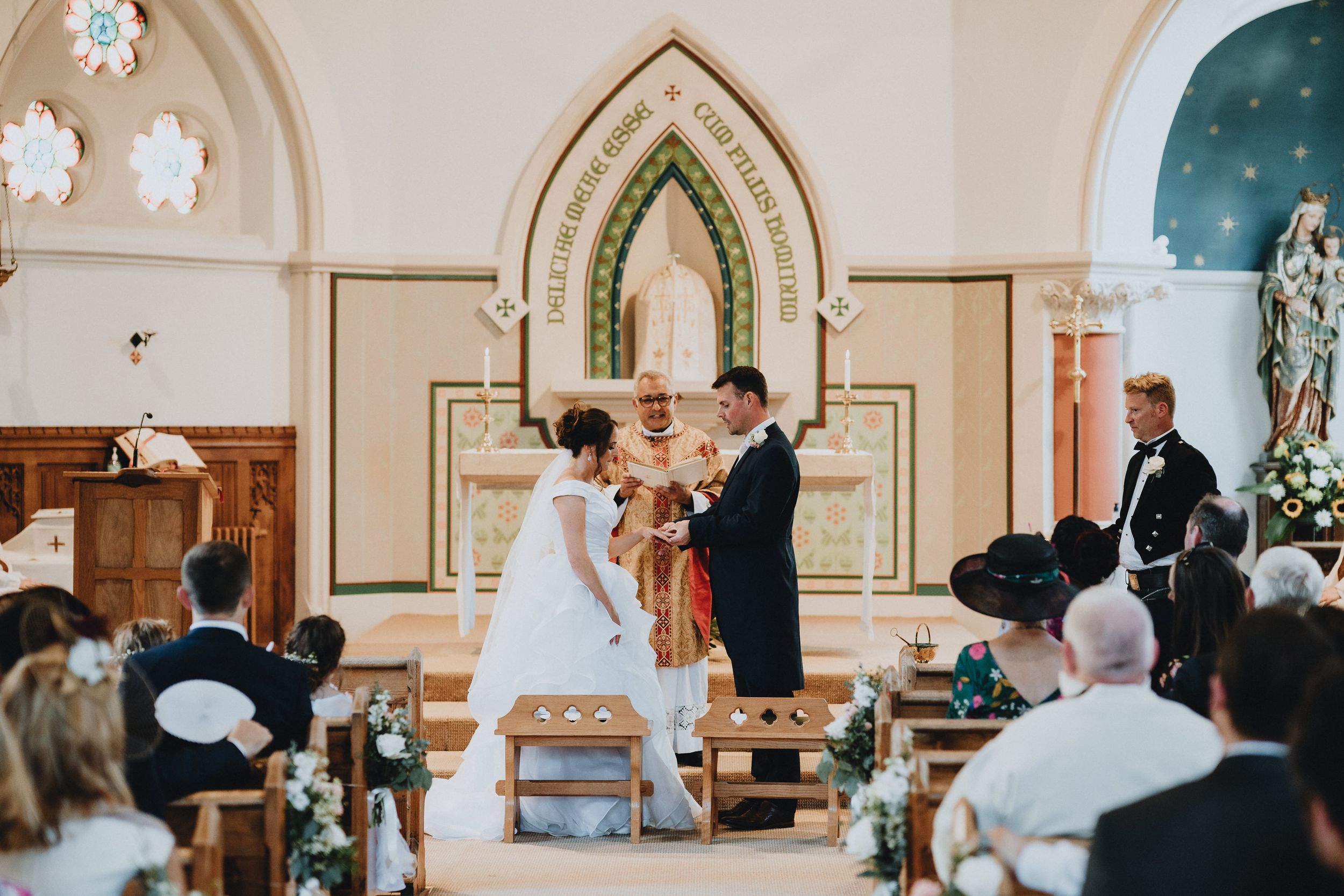 A couple exchanges vows during their wedding ceremony inside a beautiful traditional church with gothic arched windows.