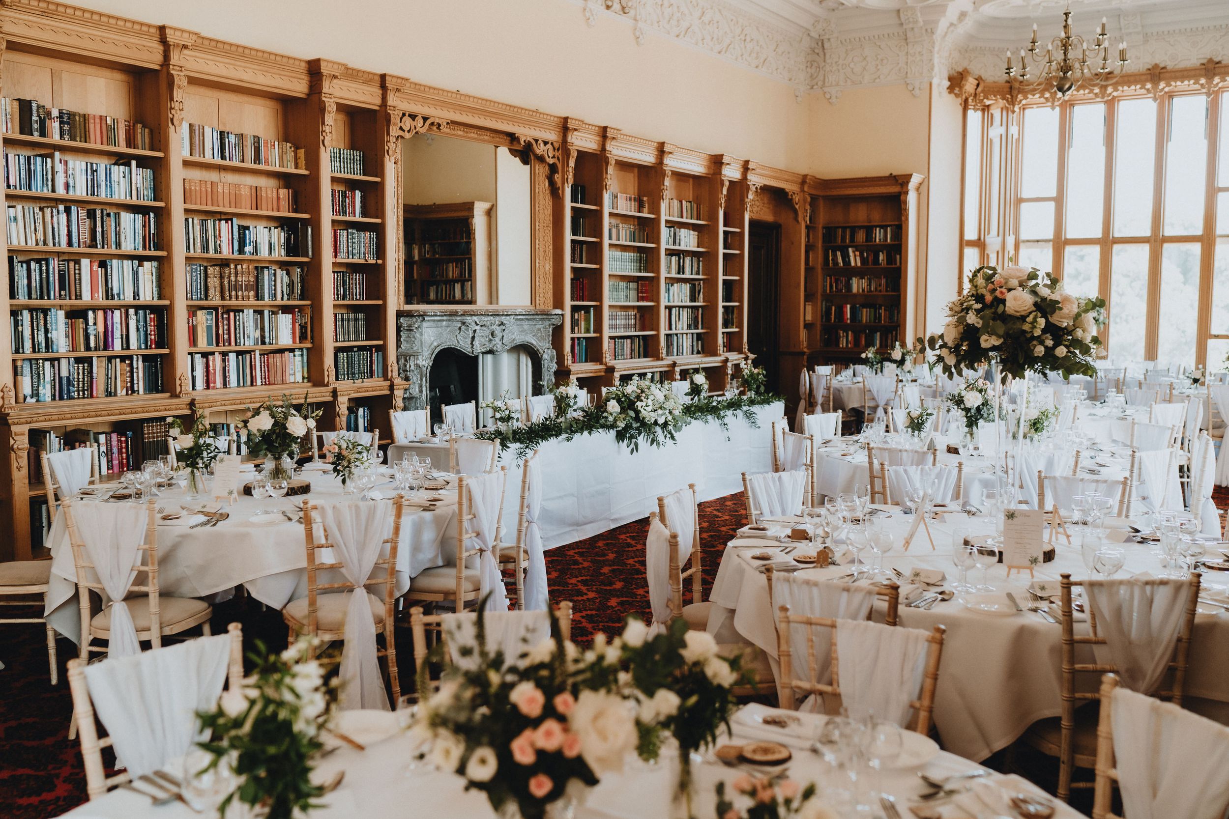 Wedding reception at Stoke Rochford Hall setup in a library room with floor-to-ceiling bookshelves and round tables.